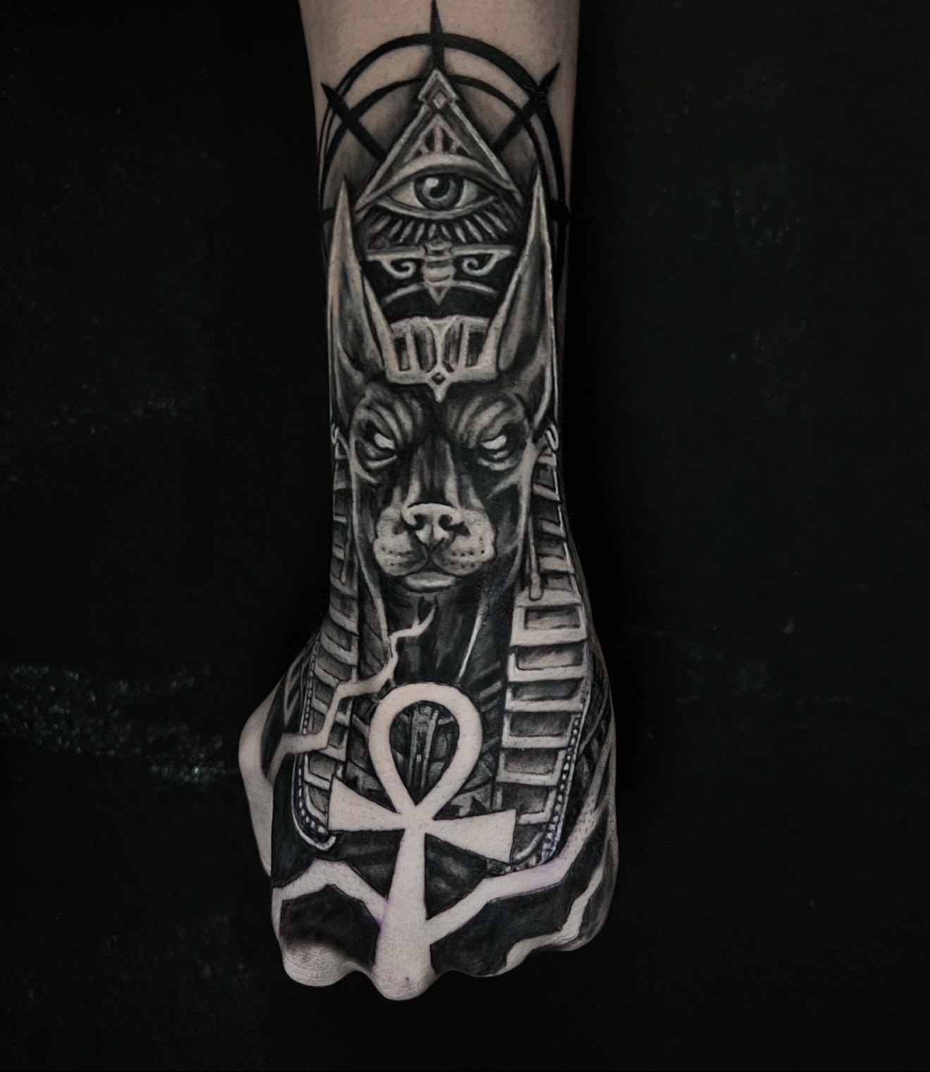 Tattoo of a dog with Egyptian-themed symbols on a person's forearm.
