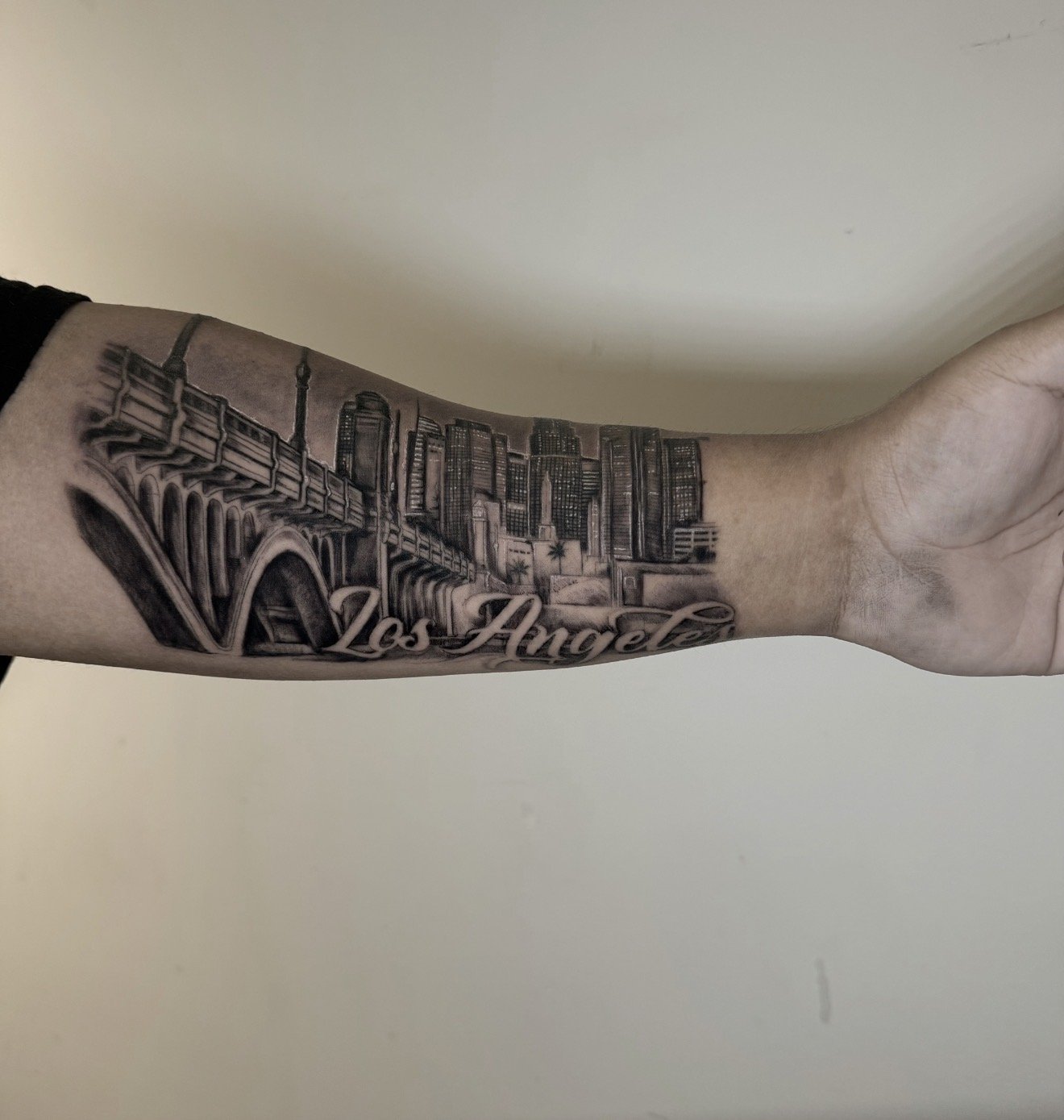 Tattoo of Los Angeles skyline and bridge on person's forearm.