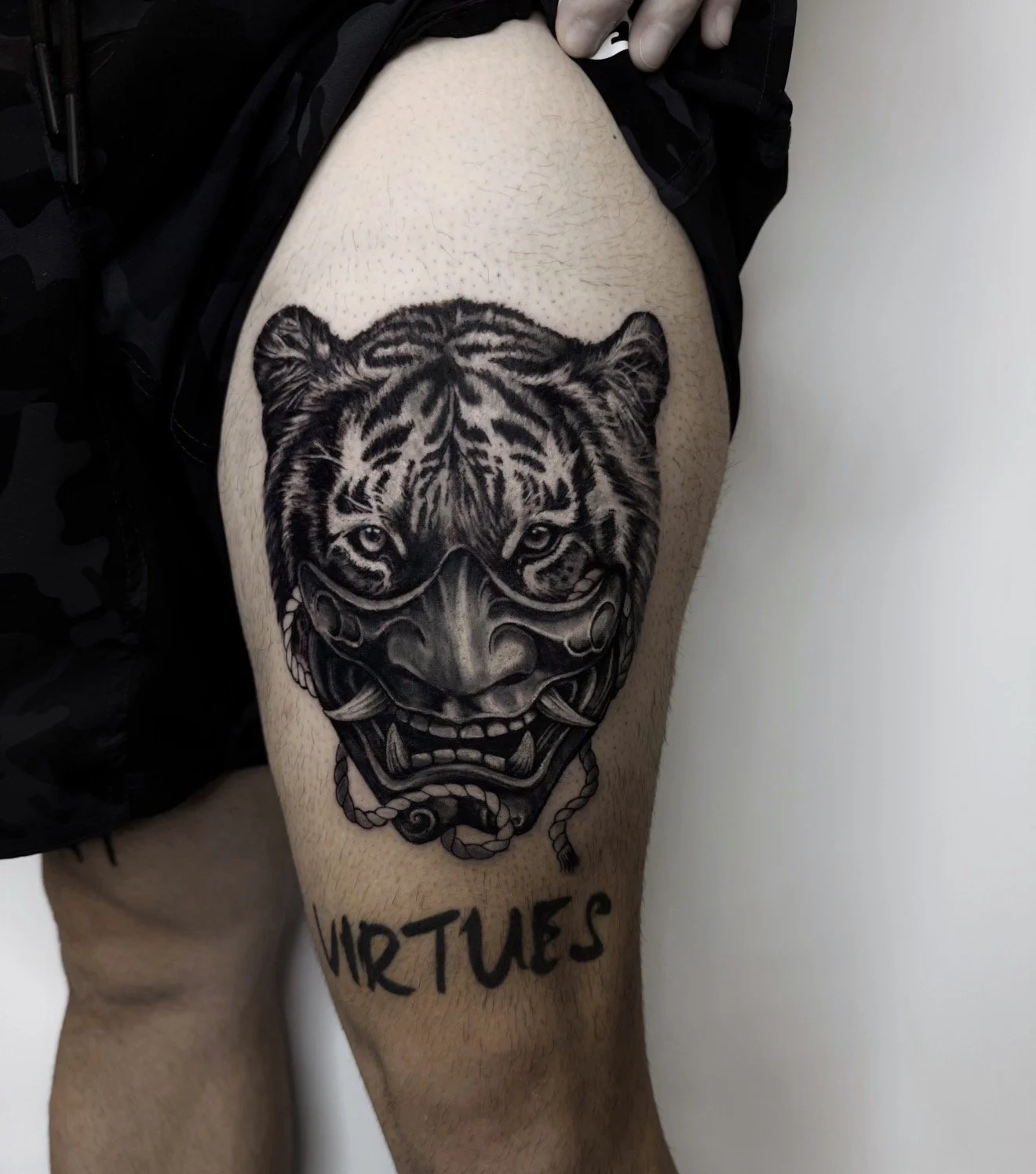 Tattoo of a tiger's face with a traditional Asian-style dragon or tiger mask design on a person's thigh.
