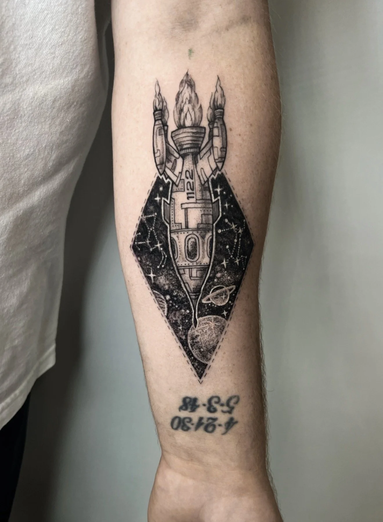 Tattoo of a spaceship launching with flames, set against a starry space background, on a person's forearm.
