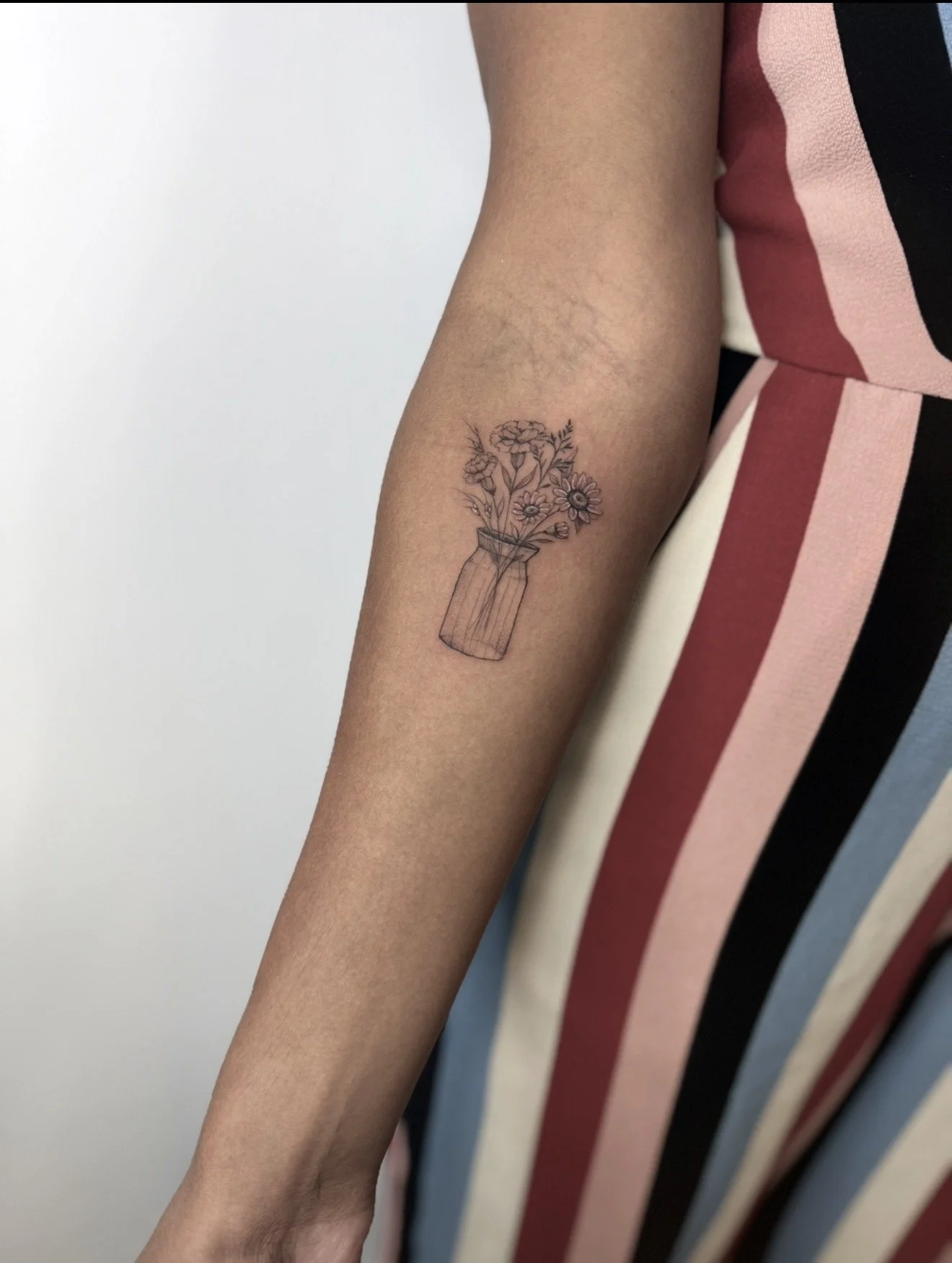 A person's arm with a tattoo of a jar holding flowers in black ink.
