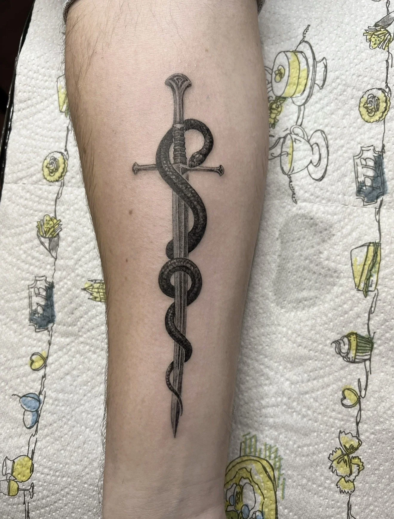 Tattoo of a snake entwined with a sword on a person's arm.