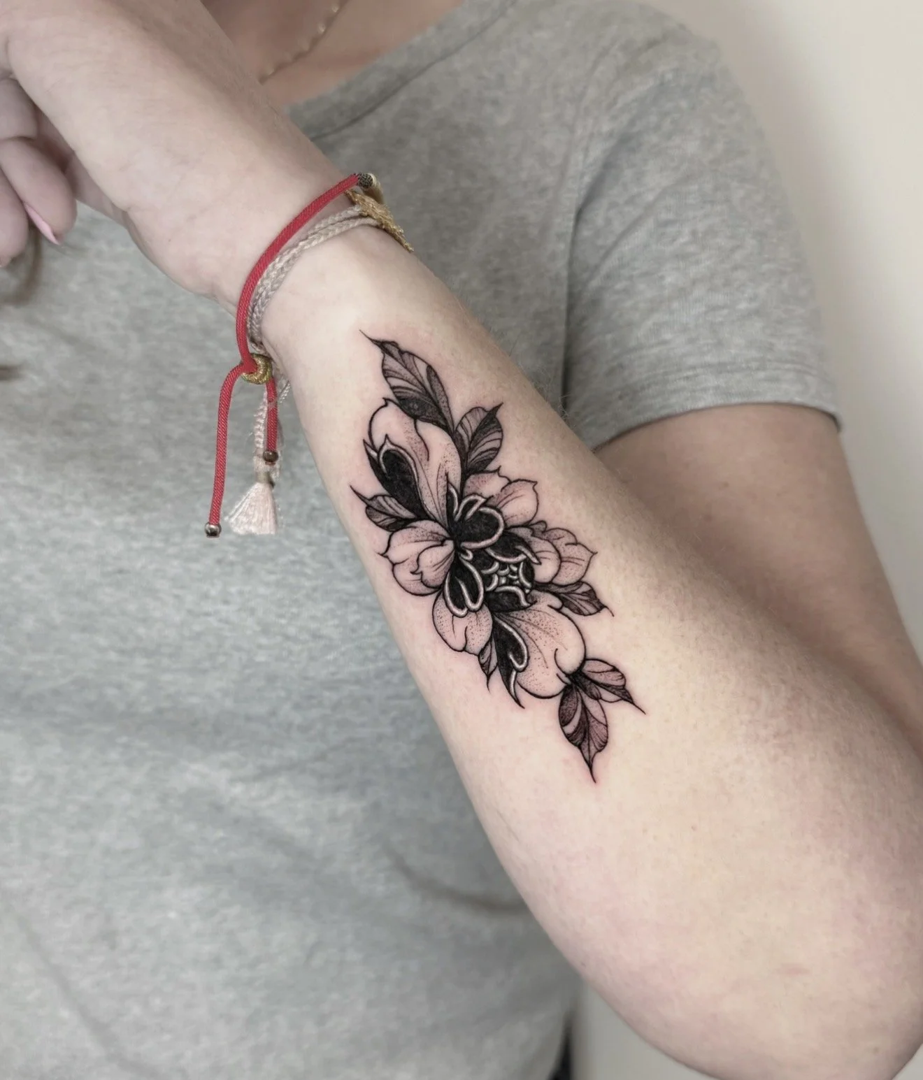 A person's forearm with a black and pink floral tattoo, wearing bracelets and a gray shirt.