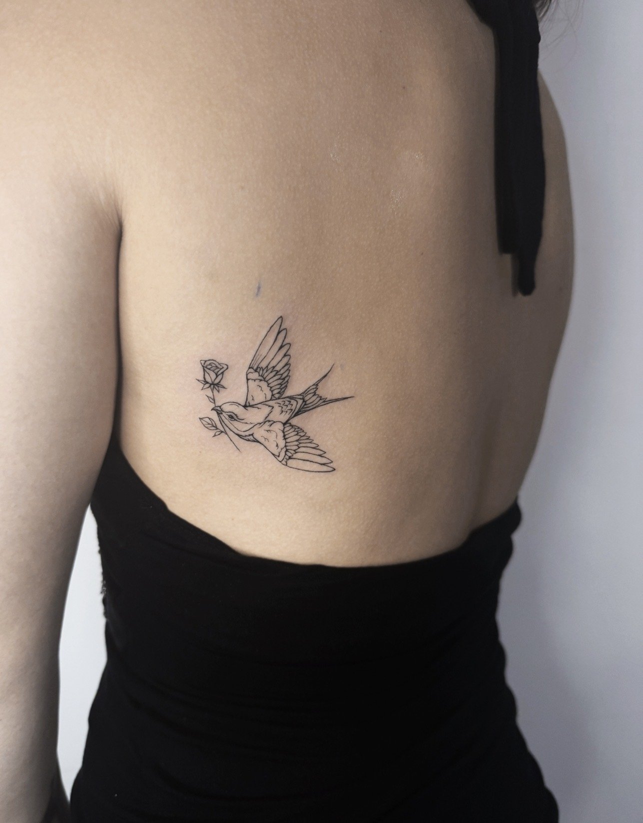 A person with light skin has a tattoo of a bird holding a rose and a branch on their side.