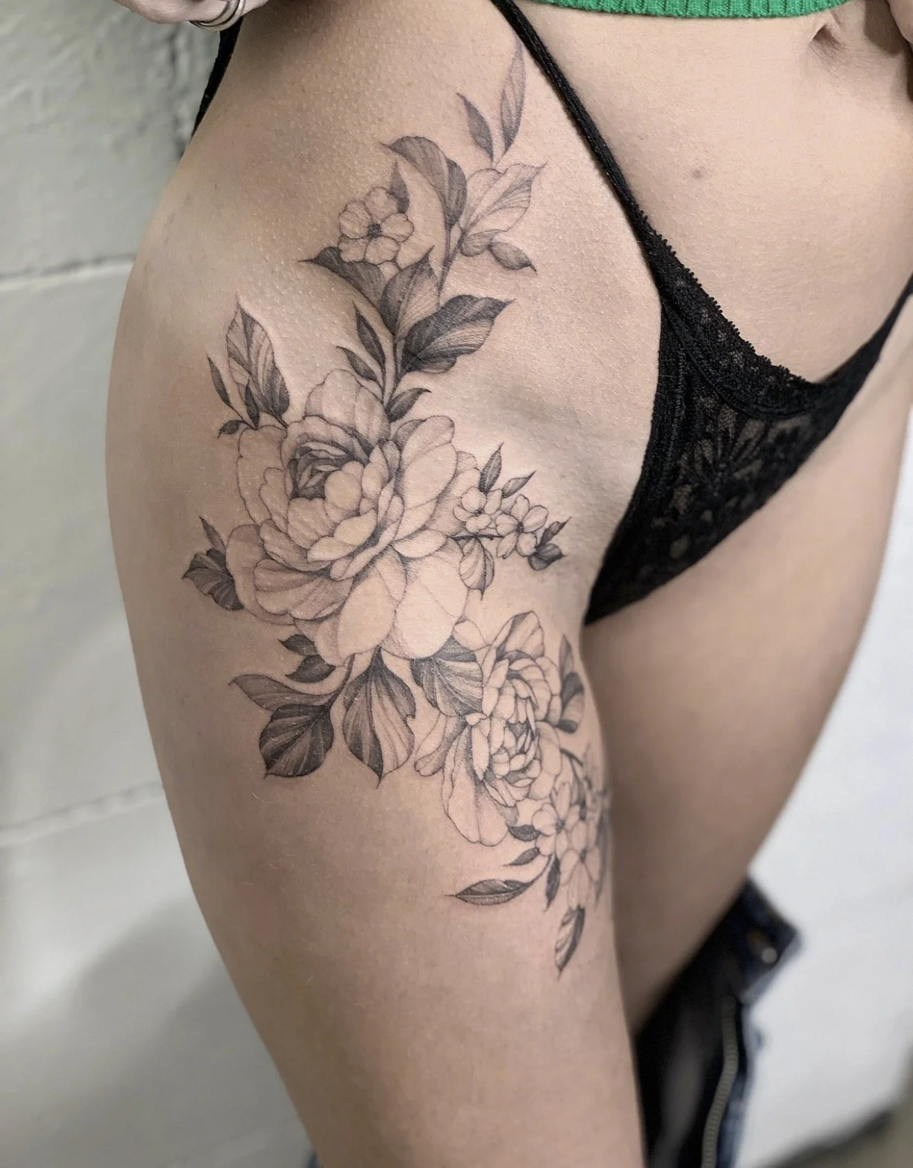 Black and gray floral tattoo on a person's upper arm and shoulder, featuring detailed roses and leaves.