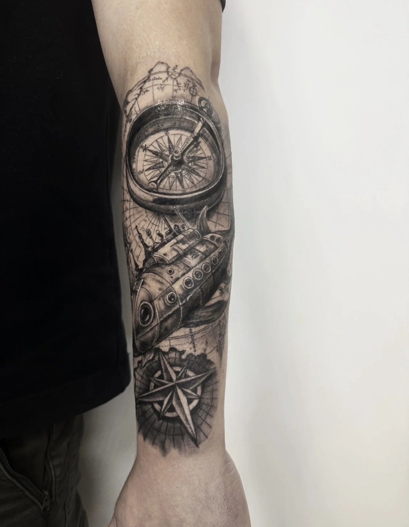 Tattoo of a detailed compass with a map in the background, located on a person's forearm.