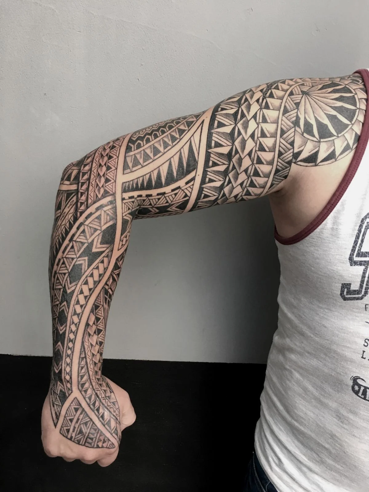 A person with a full arm tattoo featuring traditional Polynesian tribal patterns and geometric designs, extending from the shoulder to the wrist.