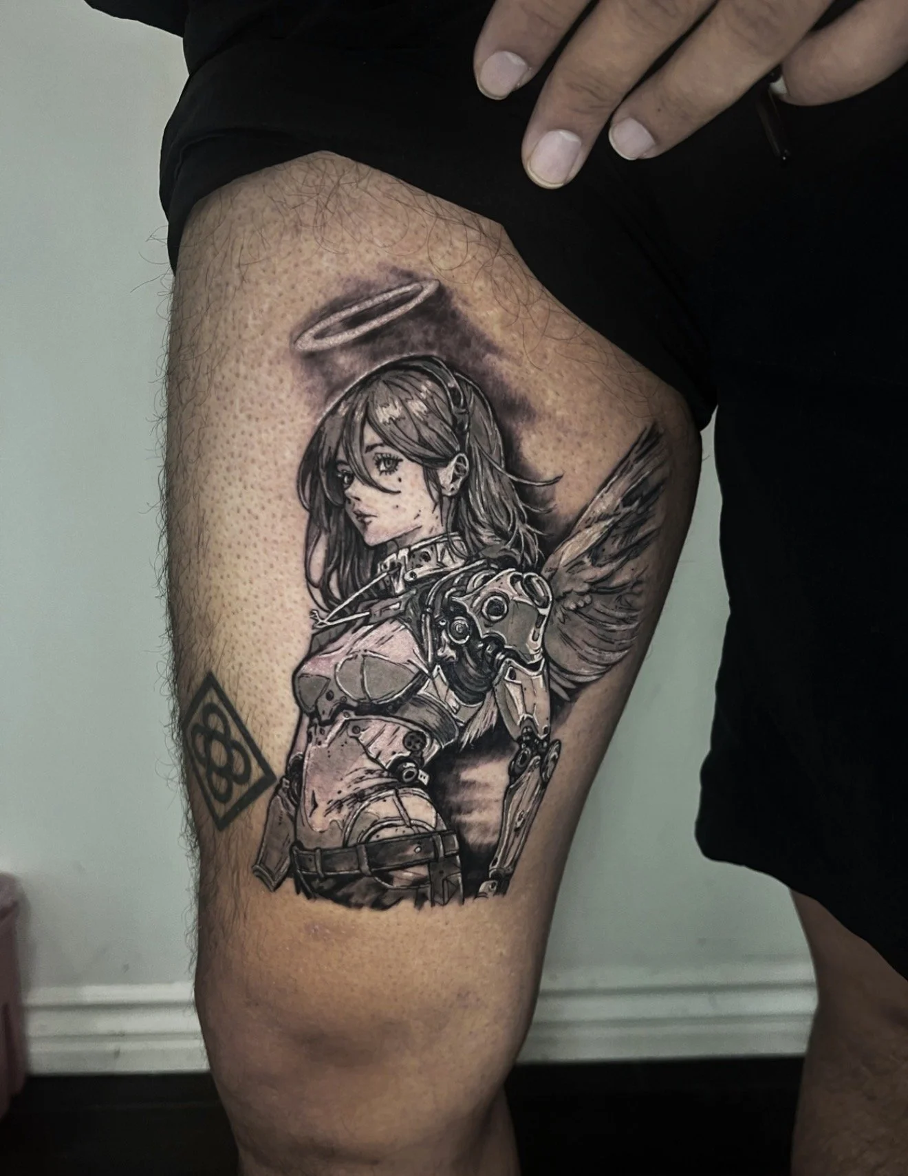 Tattoo of a female character in a robotic suit, with long hair and a halo, on a person's thigh.