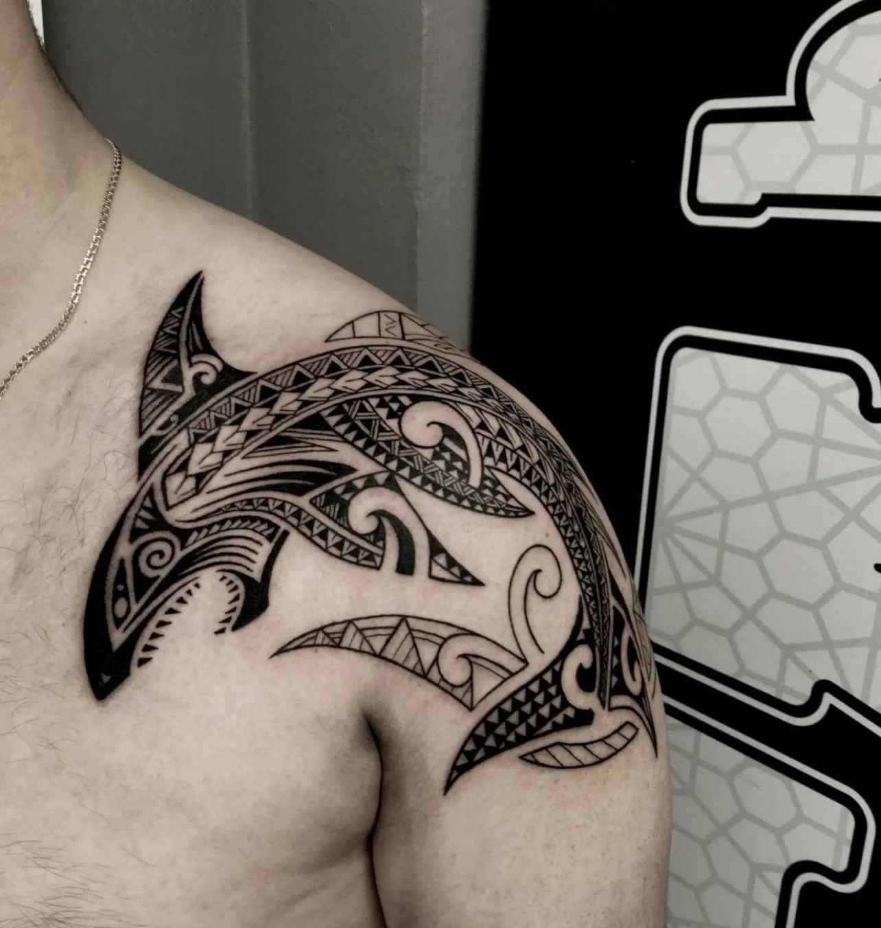 Close-up of a person's shoulder and upper arm featuring a Polynesian tribal tattoo design.