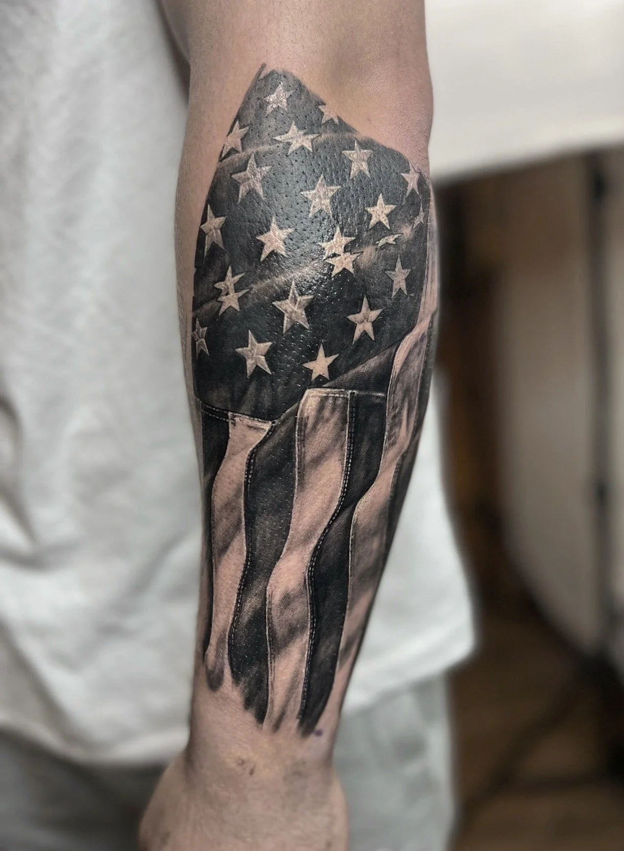 Tattoo of a waving American flag on a person's forearm.