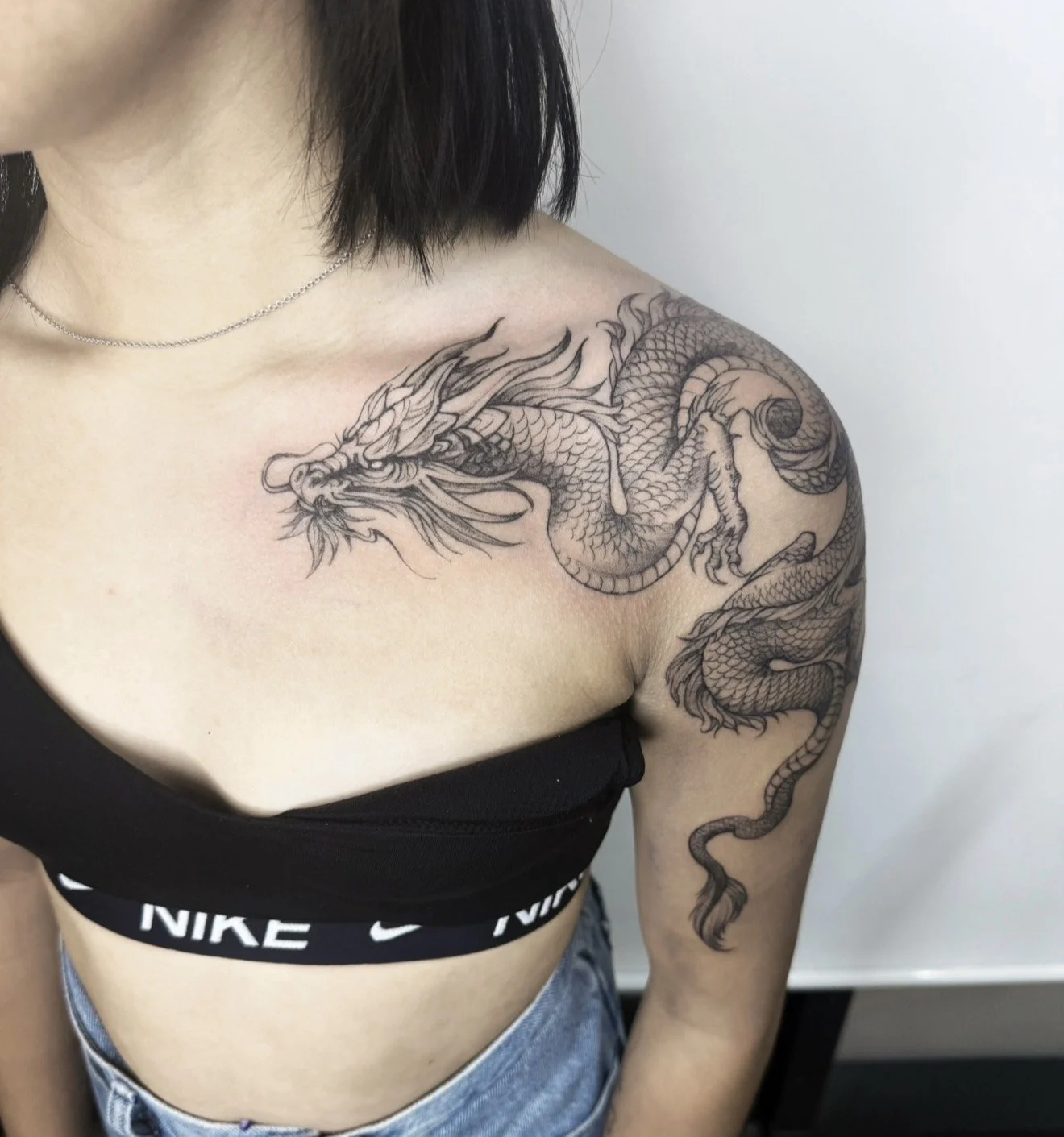 Black and gray tattoo of a dragon on a woman's shoulder and upper arm.