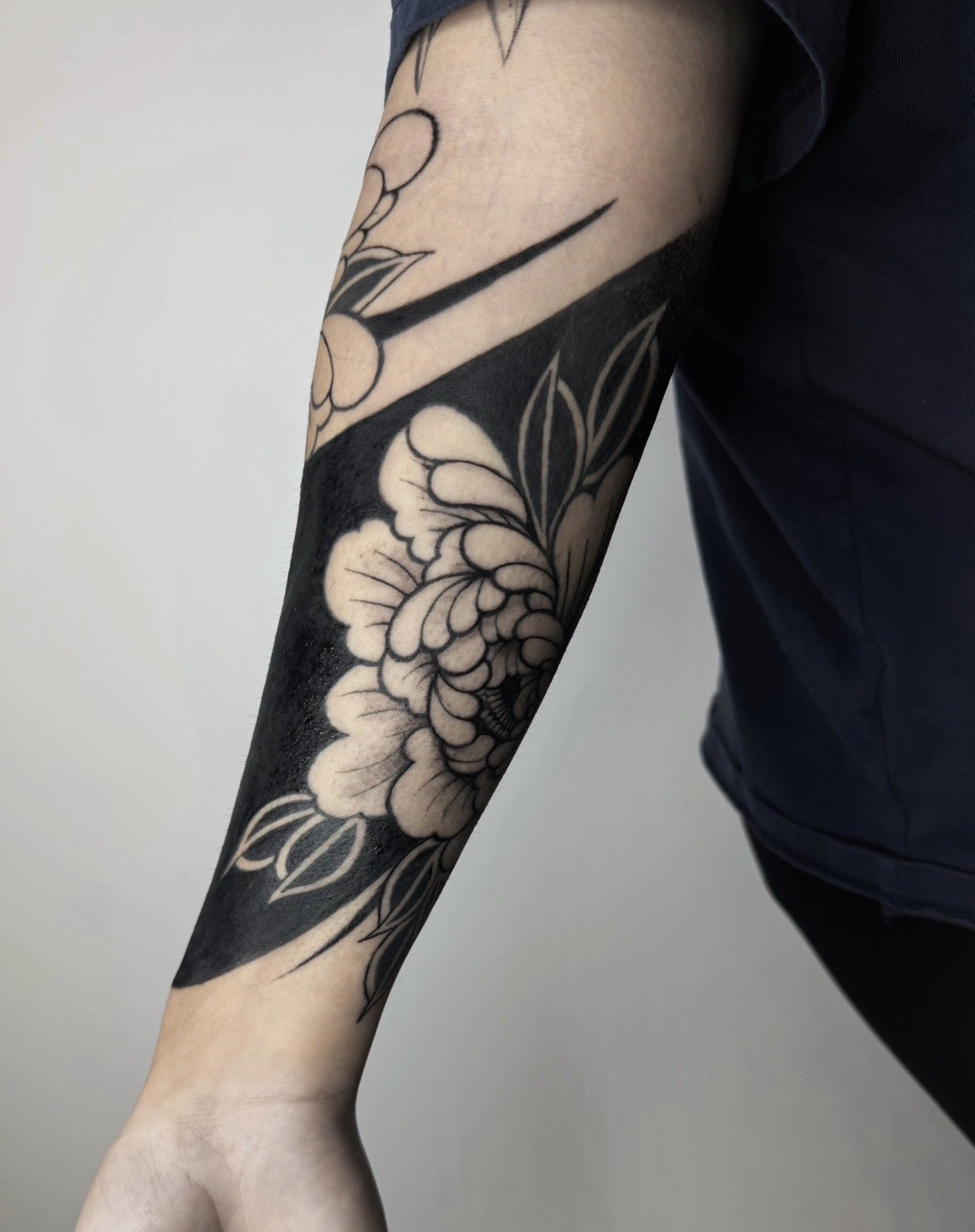 A person's arm with a black and white floral tattoo extending from the shoulder to the forearm.