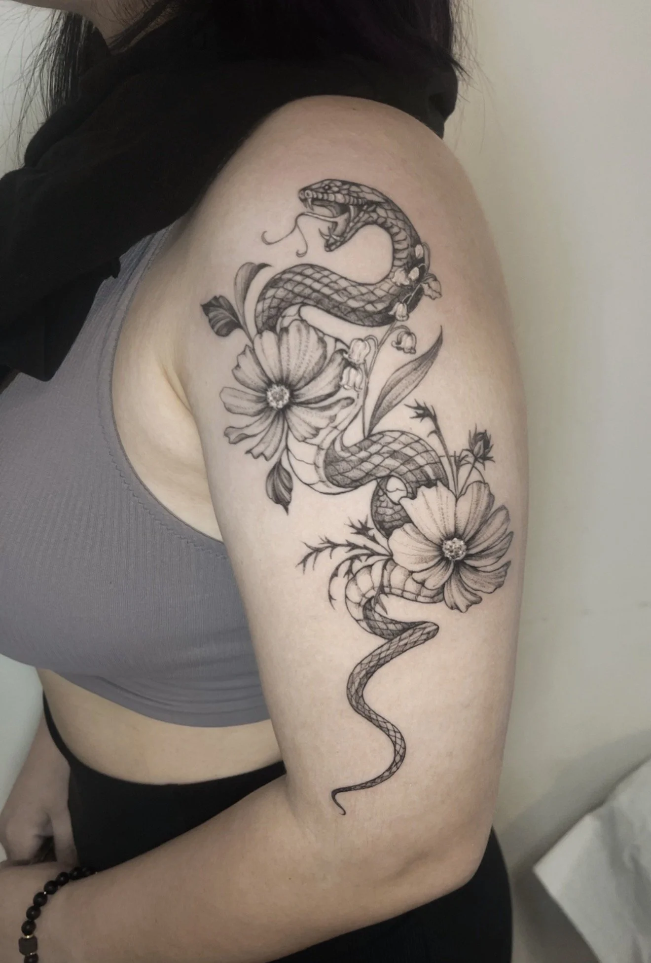 Tattoo of a snake intertwined with flowers on a person's upper arm.