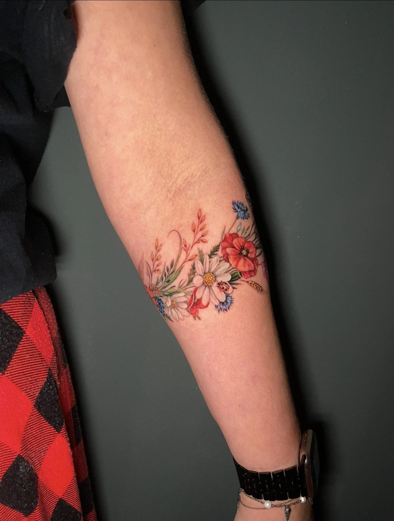 A person's arm resting on a surface with a colorful floral tattoo featuring various flowers in vibrant colors.