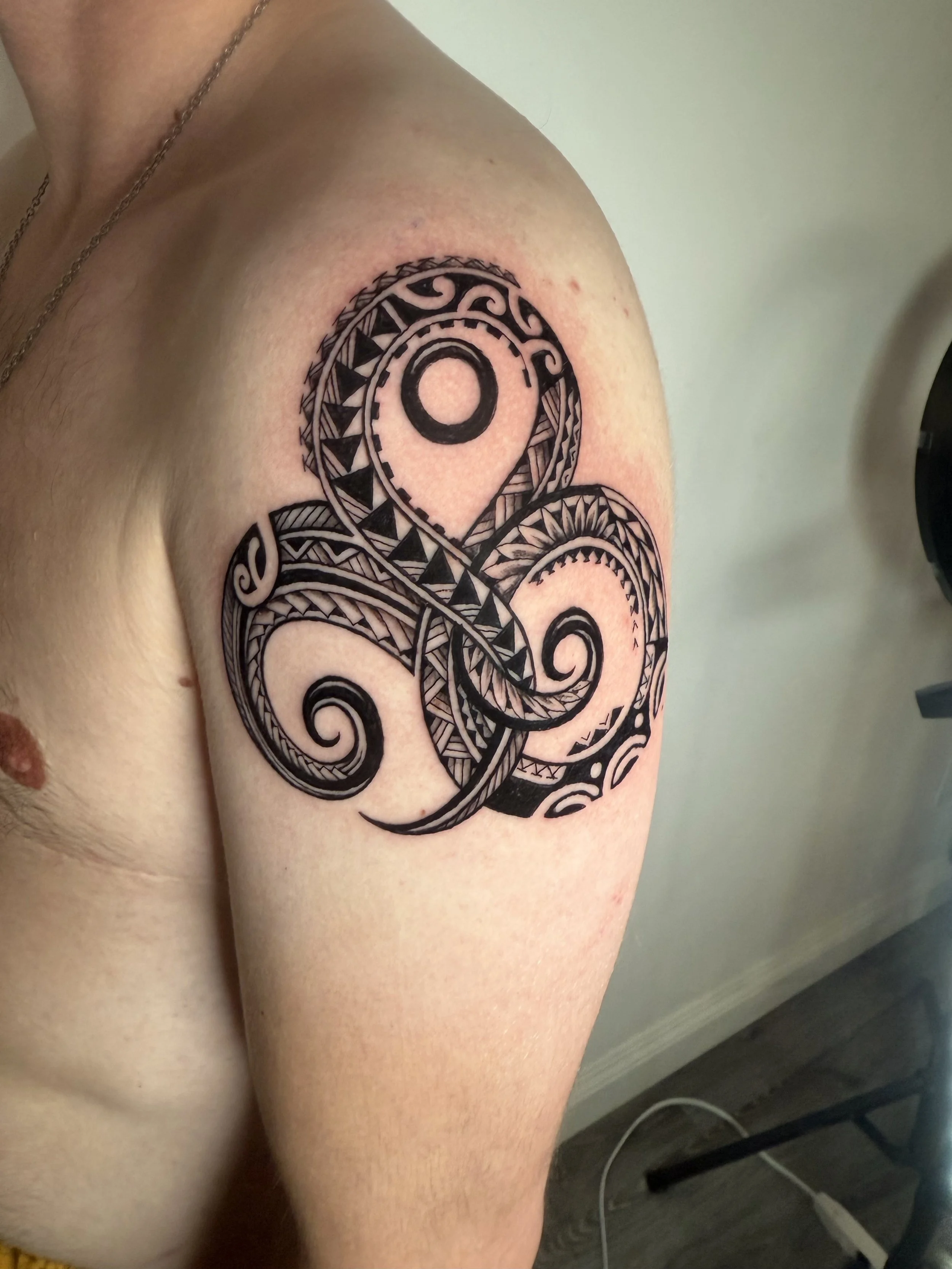 A black tribal style tattoo on a person's shoulder and upper arm, featuring swirling patterns and geometric shapes.