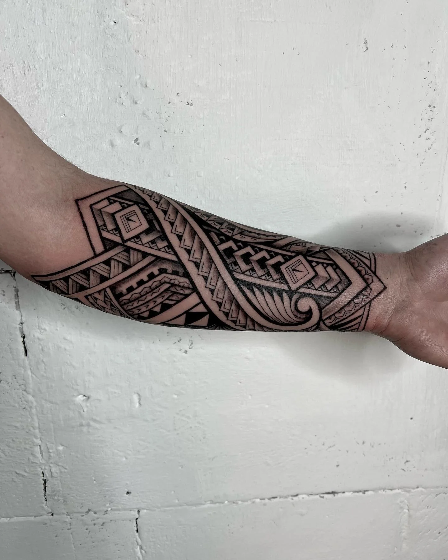A person's forearm and hand with a tribal style tattoo featuring geometric patterns in black ink, extending from wrist to elbow.