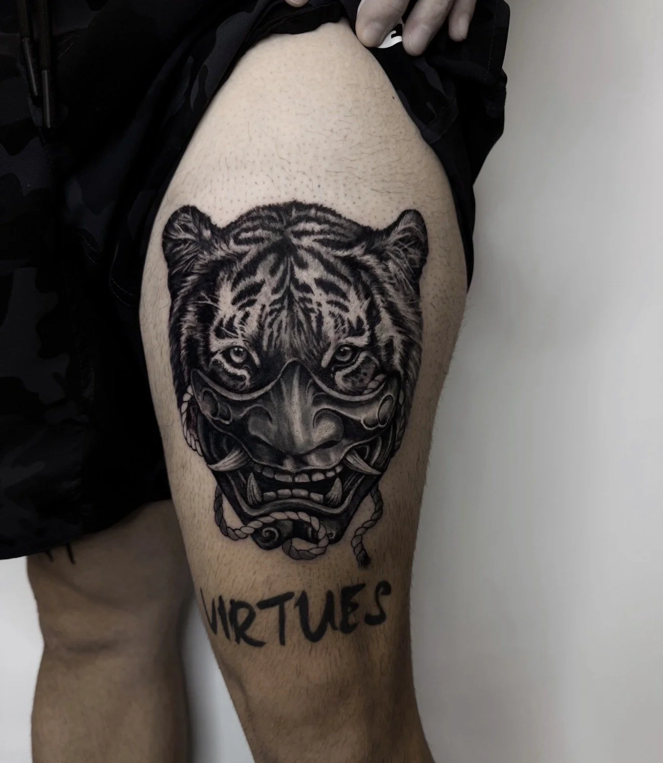 Tattoo of a tiger's face with a traditional mask design, located on a person's upper thigh.