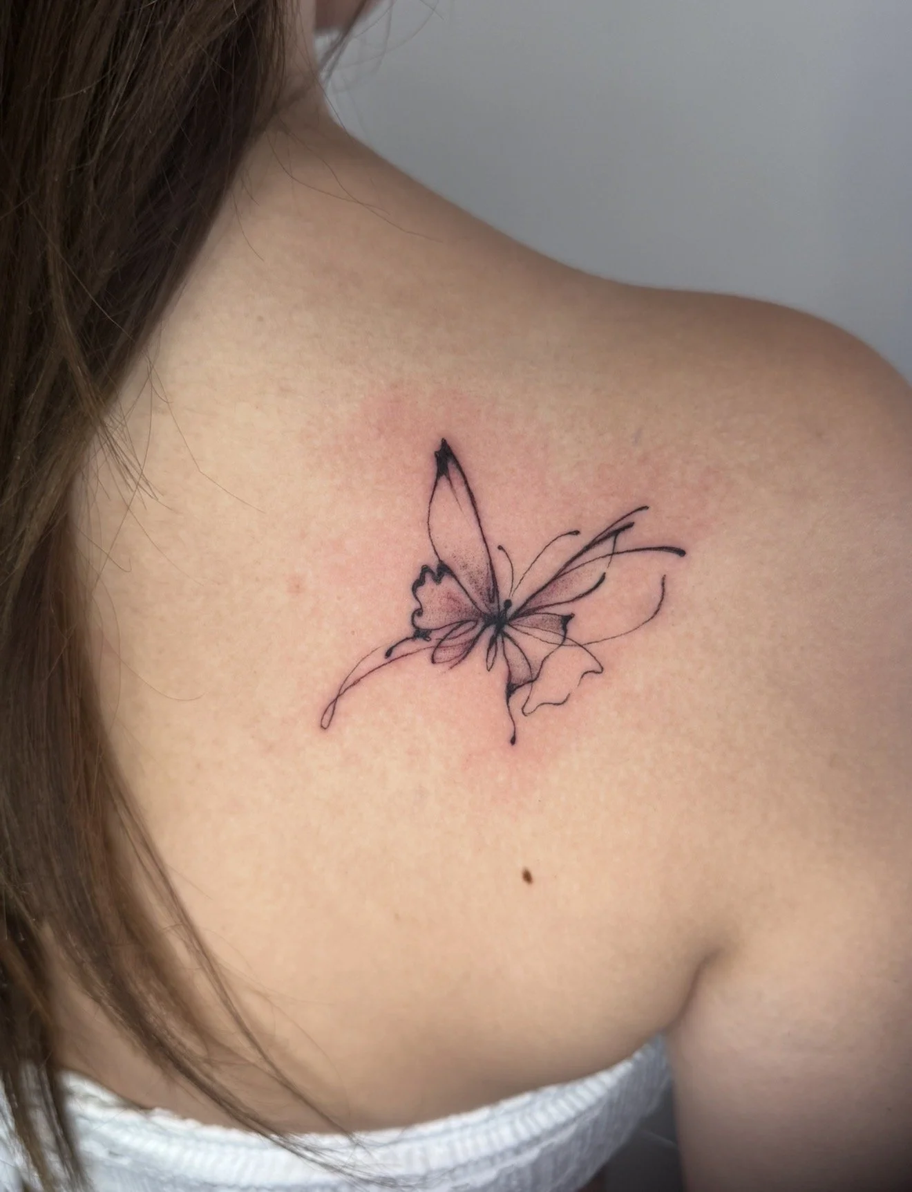 A black outline tattoo of a butterfly on the person's shoulder.