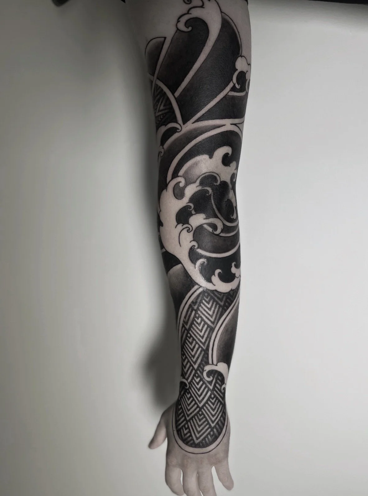 Black and gray tattoo sleeve featuring waves, clouds, and geometric patterns on a person's arm.
