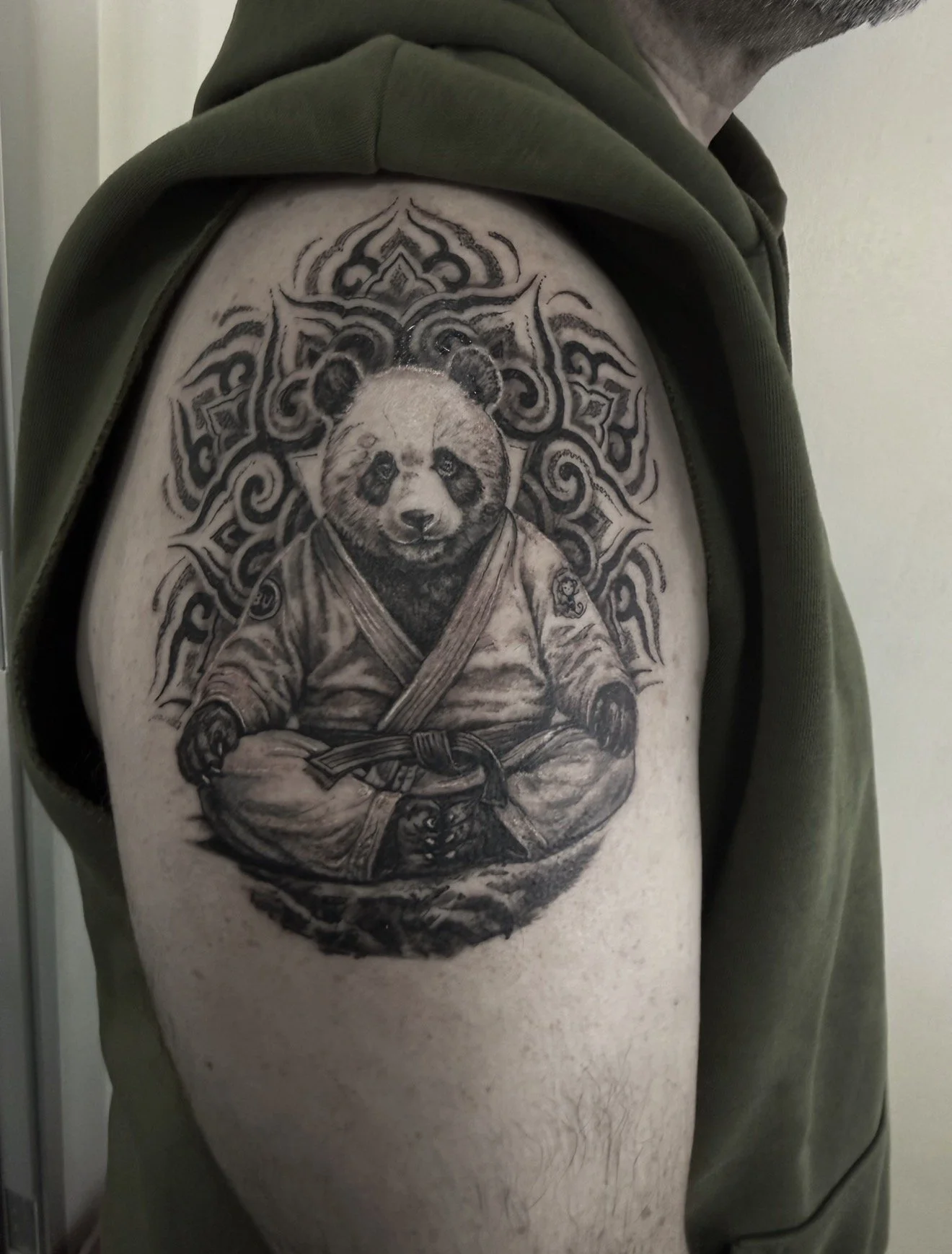 Tattoo of a panda in a martial arts outfit sitting cross-legged, with a detailed background, inked on a person's upper arm.