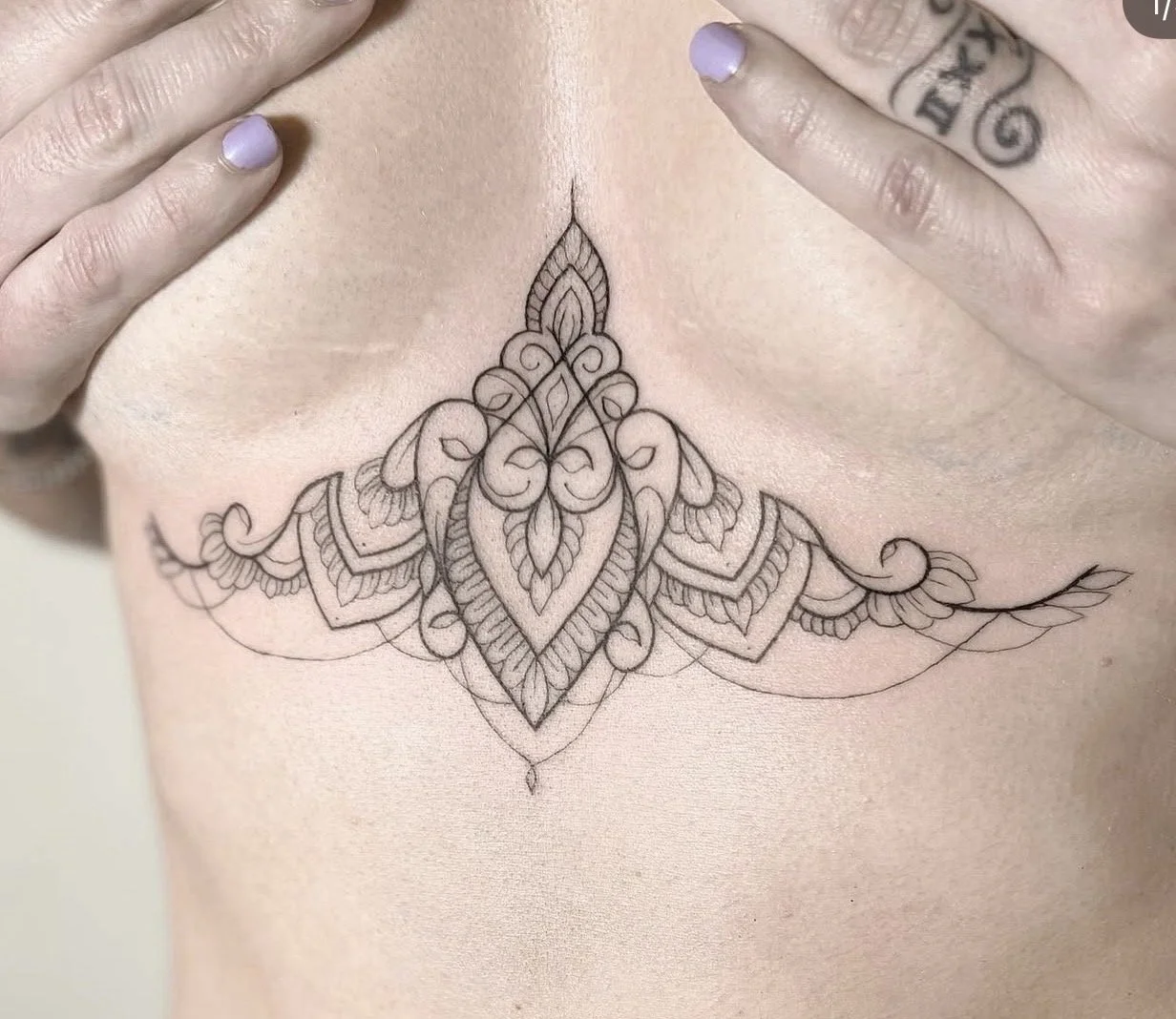 A detailed tattoo design on skin featuring symmetrical ornamental patterns with floral and leaf motifs.