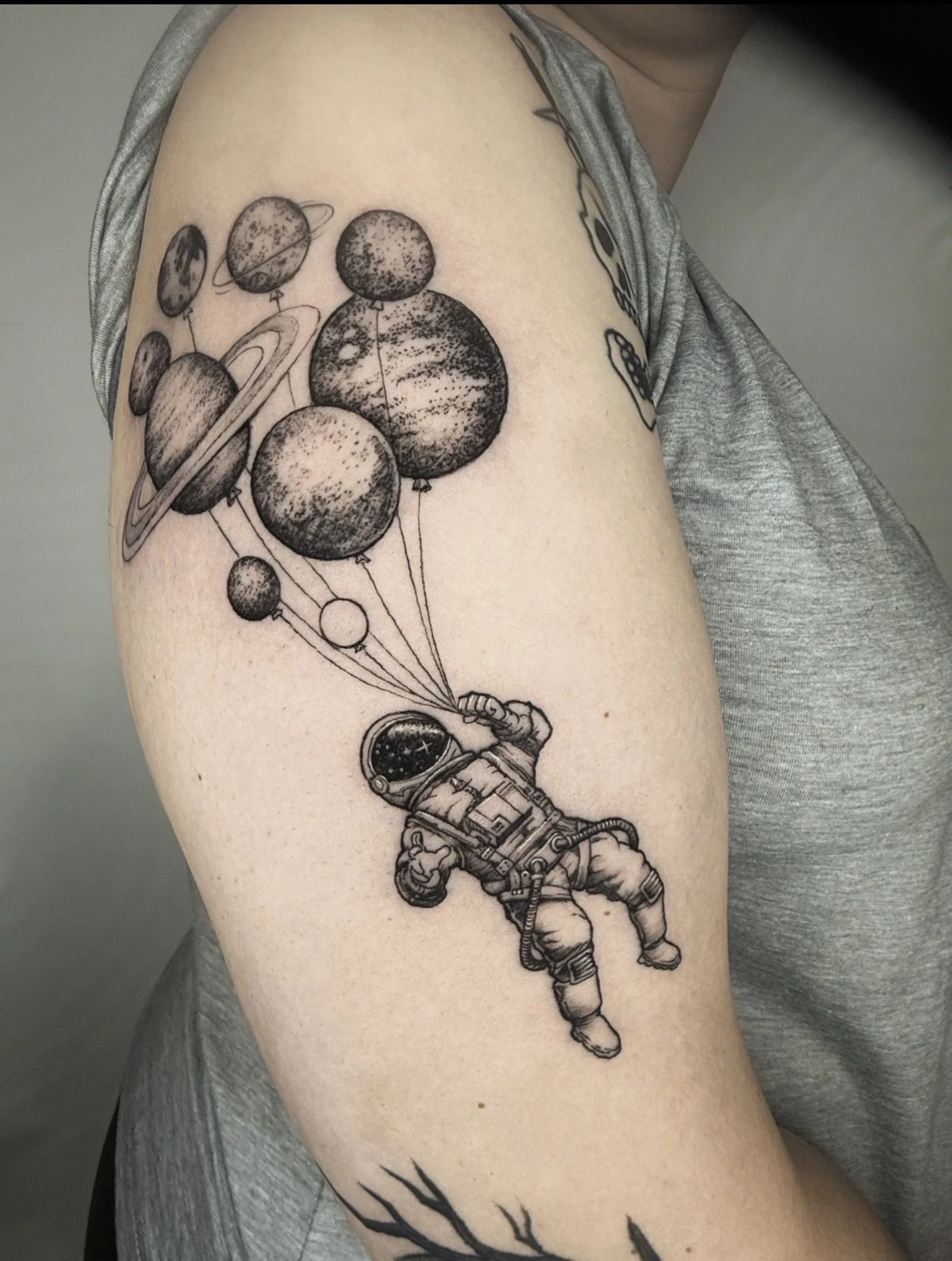 Tattoo of an astronaut floating in space holding a bunch of planets connected by strings, with stylized trees at the bottom.