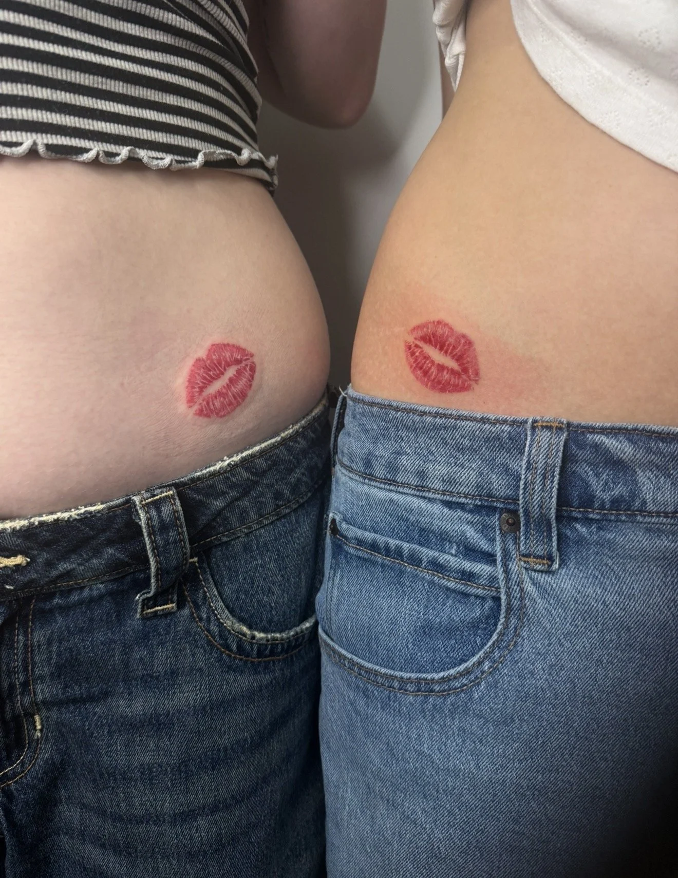Two people wearing blue jeans with lipstick kiss tattoos on their lower backs.