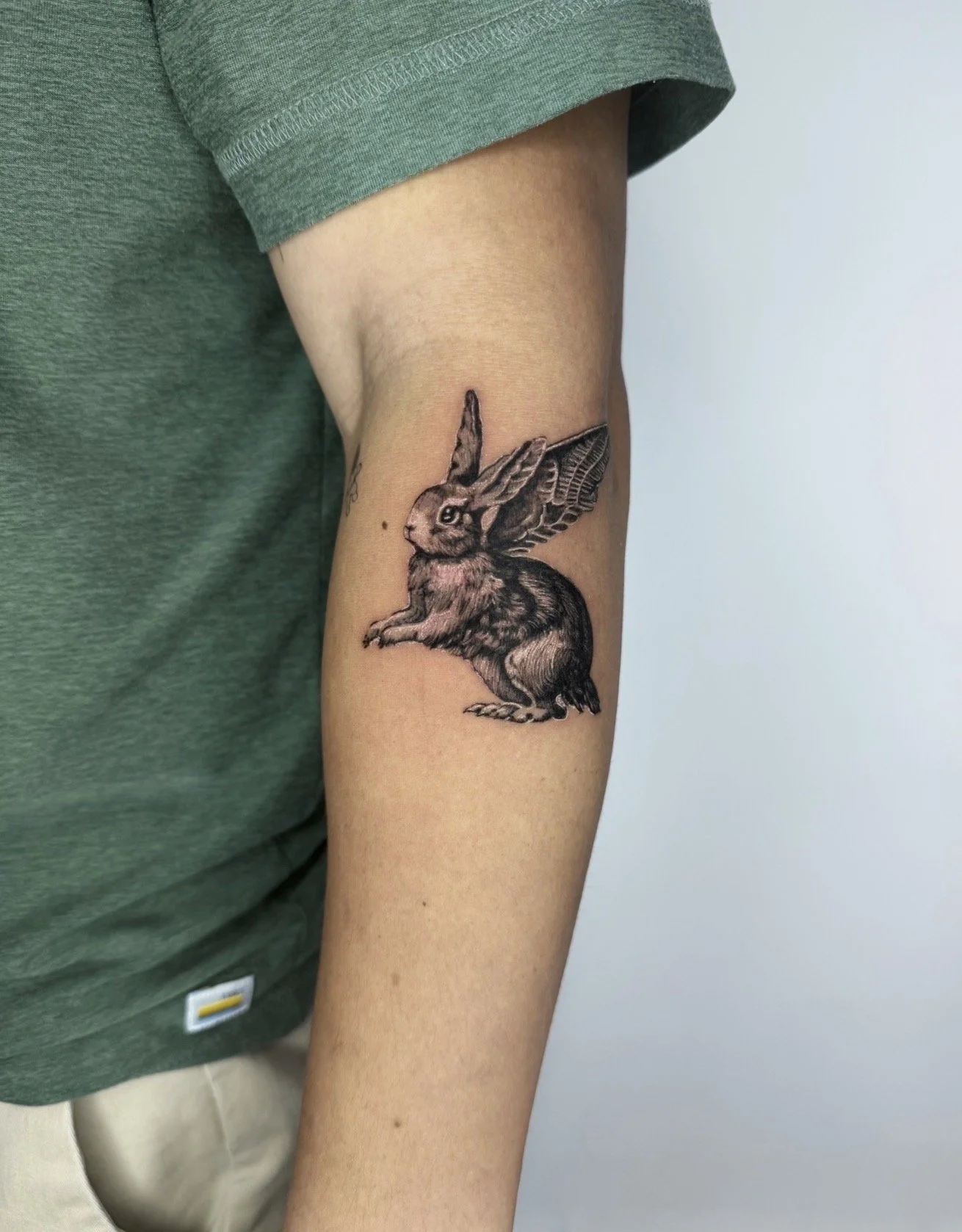 Tattoo of a rabbit with butterfly wings on a person's upper arm.