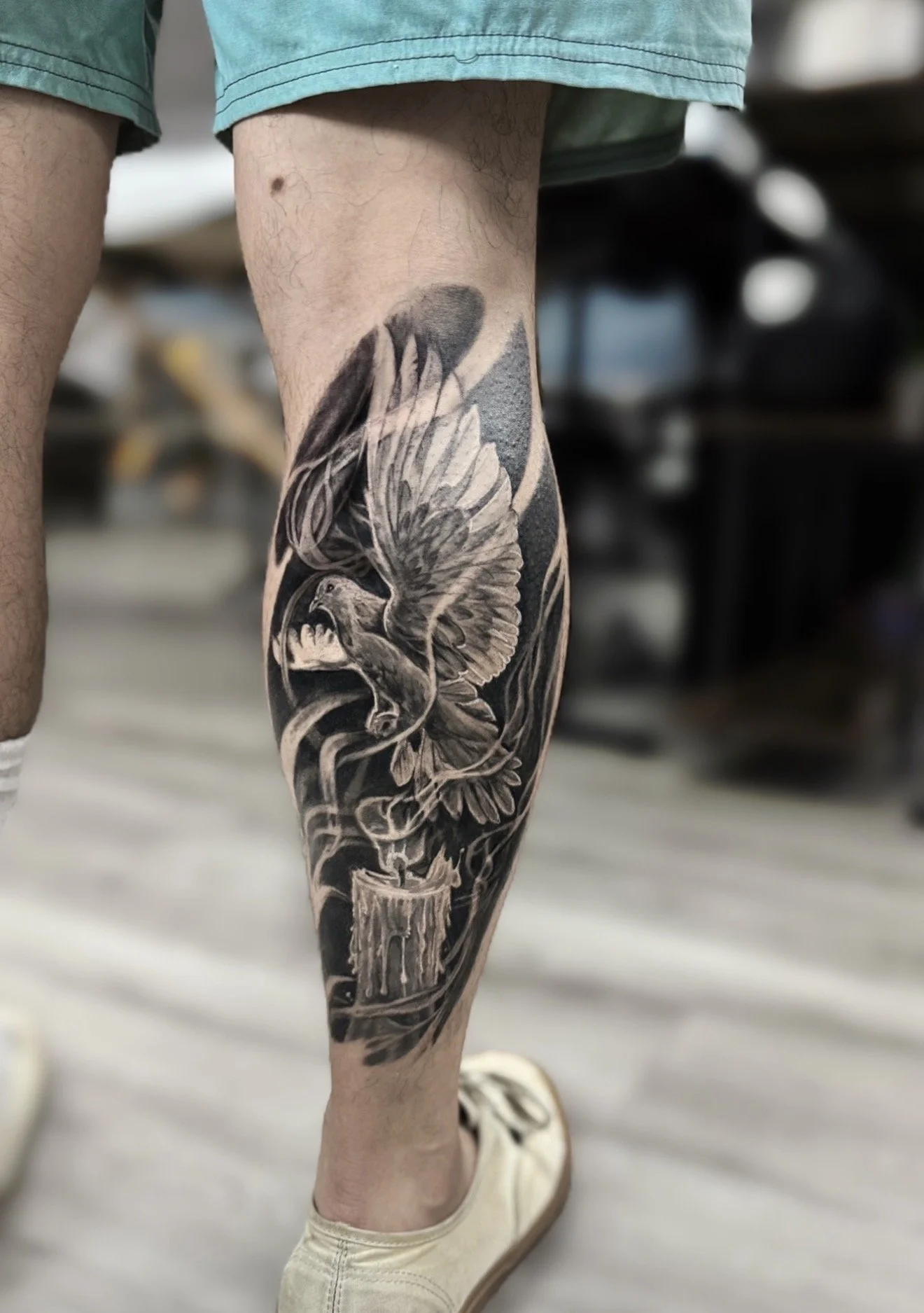 Close-up of a person’s leg with a detailed black and gray tattoo of a dragon and flames going down the calf.
