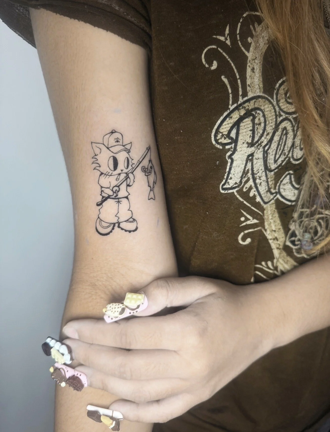 Tattoo of a cartoon cat holding a fishing rod with a fish on the line on a person's inner forearm.