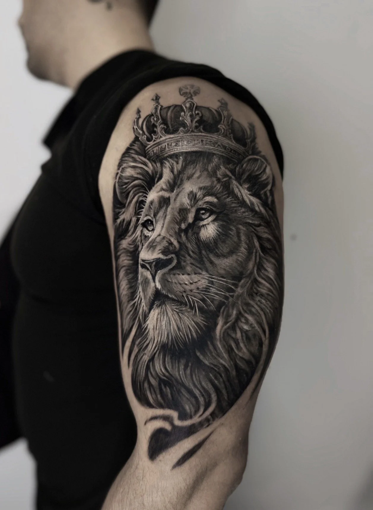 Black and grey crowned lion tattoo on upper arm