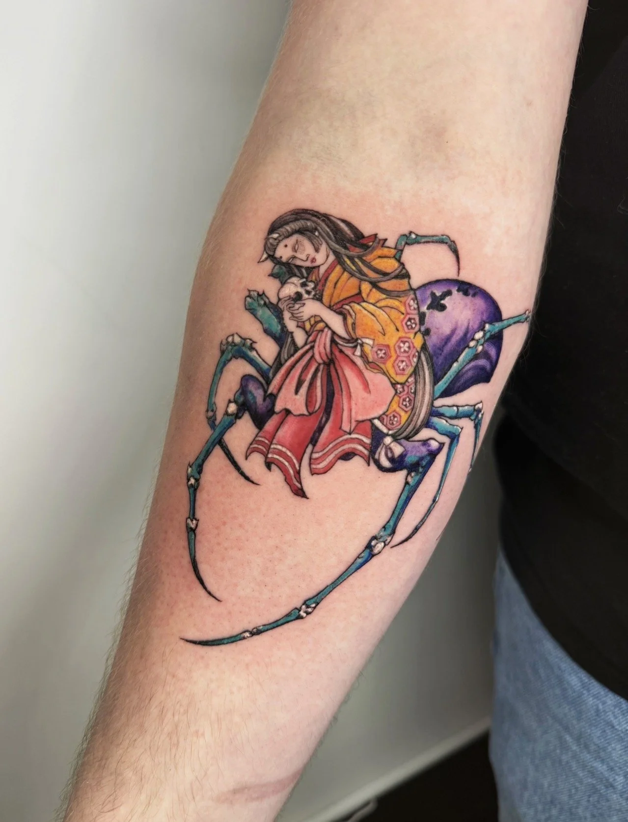 Colorful tattoo of a woman holding a skull and a spider on a person's forearm.