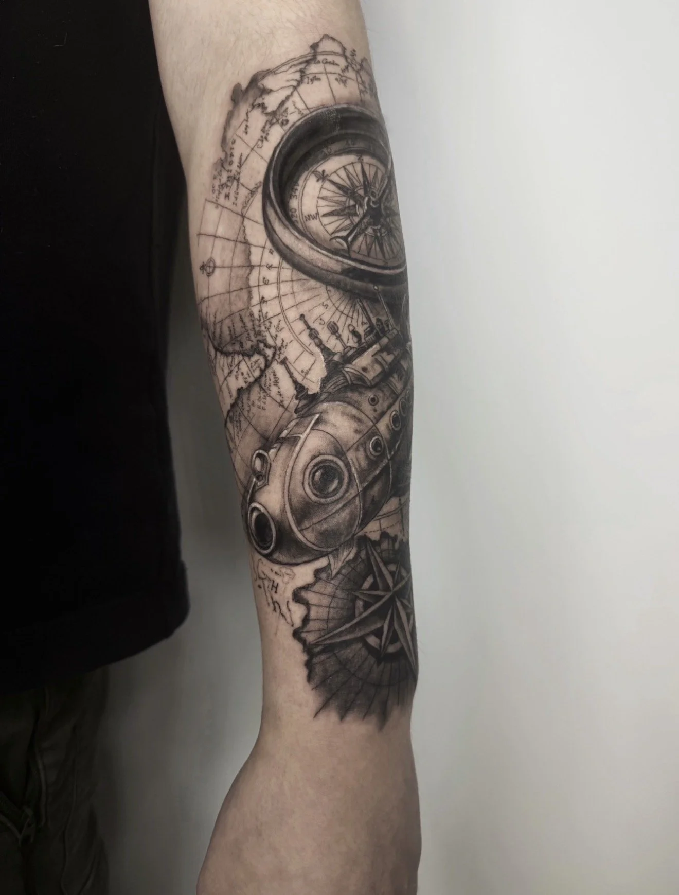 Tattoo of a compass, a map, and a gun on a person's forearm
