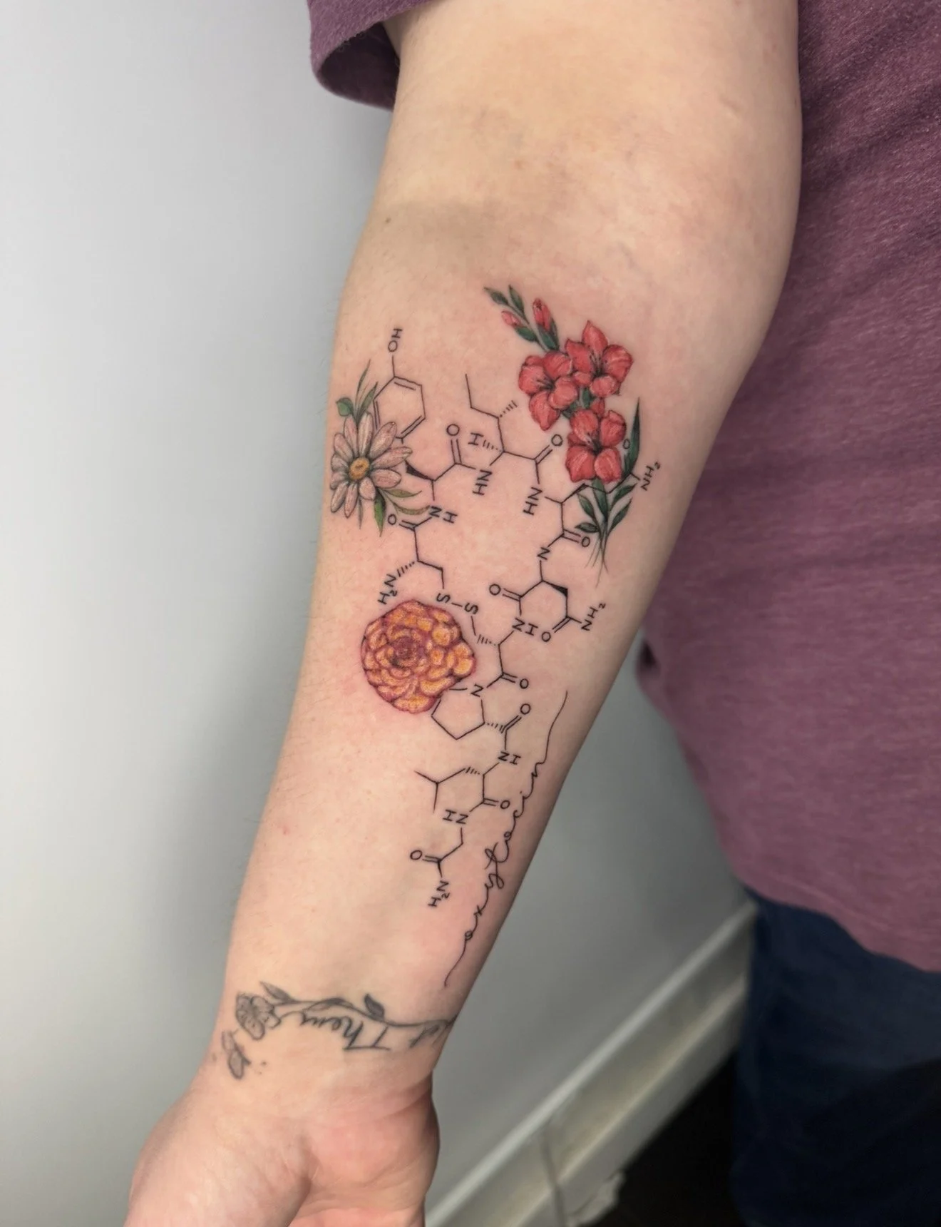 Tattoo on person's arm depicting a chemical structure intertwined with colorful floral designs, including pink and orange flowers, with some greenery.