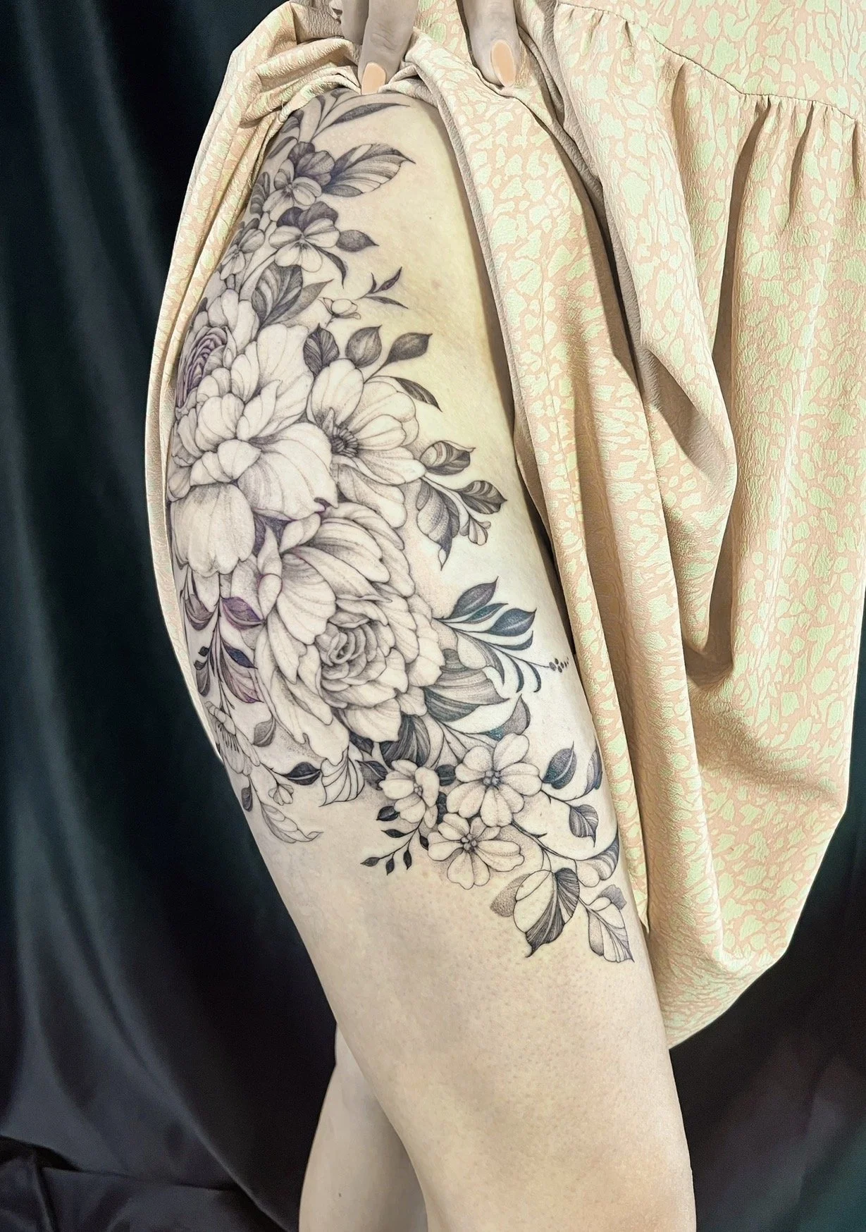 A person's arm with a detailed black and white floral tattoo featuring large flowers and foliage.