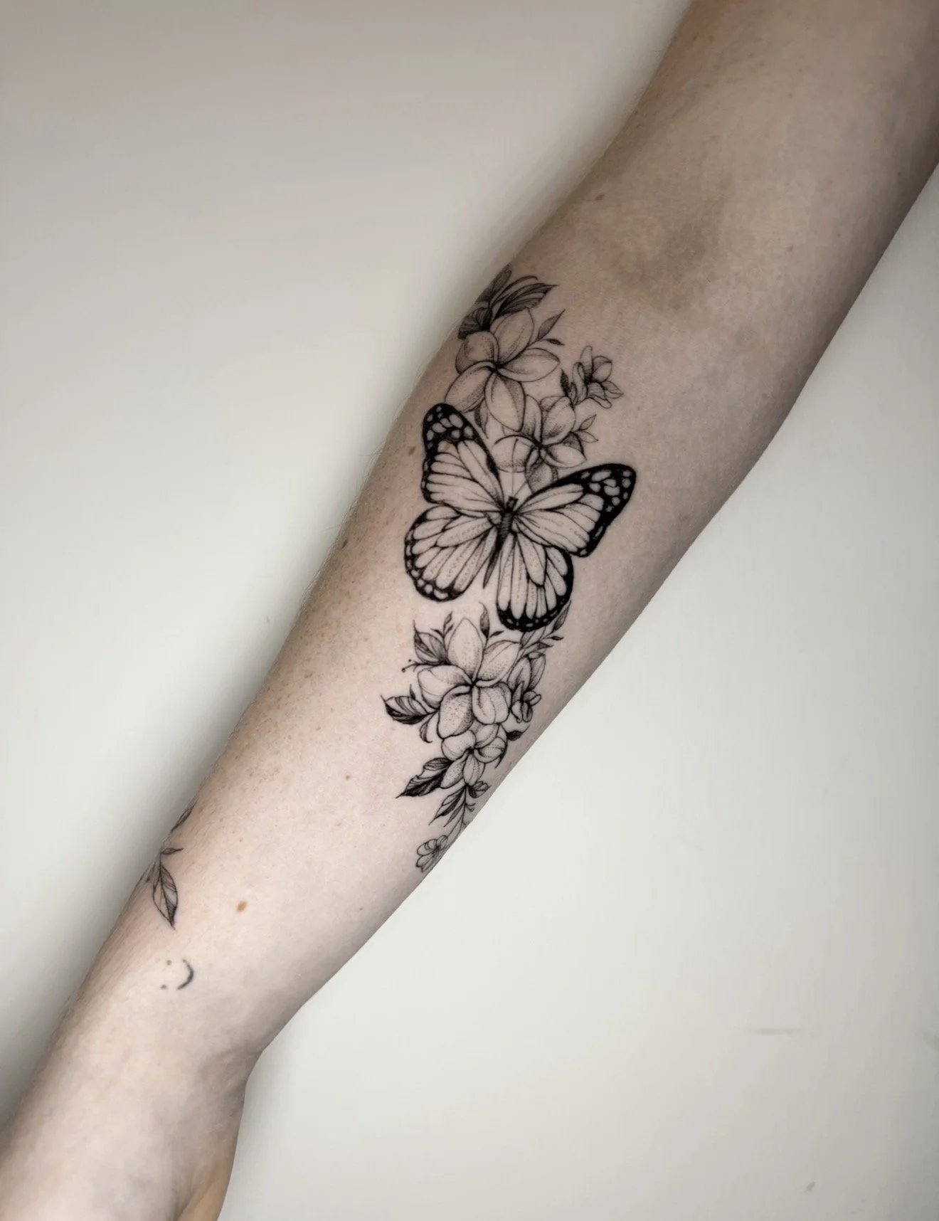 A person's forearm with a black and white floral tattoo featuring a butterfly and flowers.