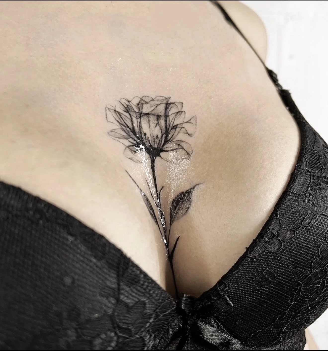 Black floral tattoo on person's chest, partially covered by black lace fabric.