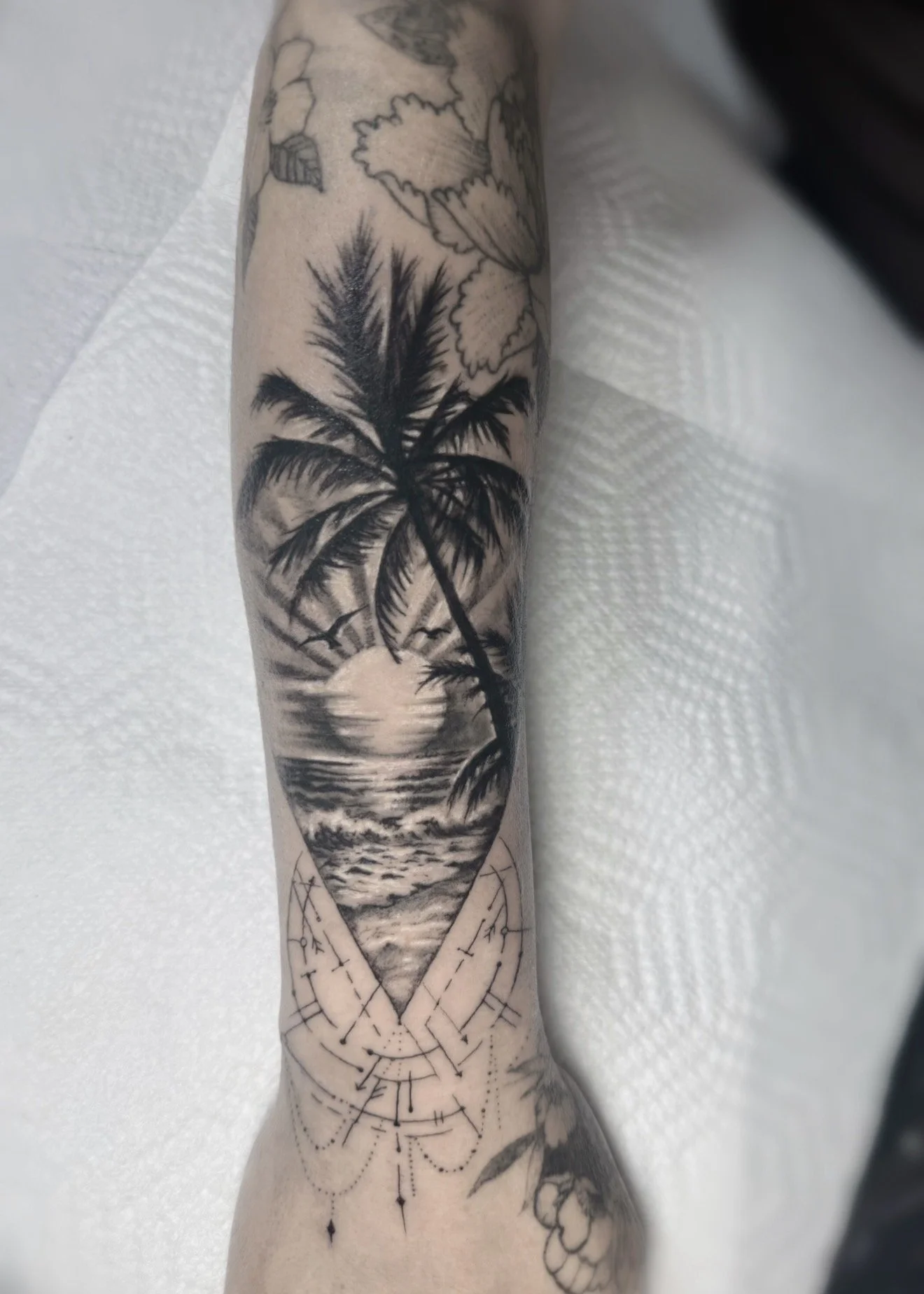 Tattoo of a sunset over the ocean with a palm tree silhouette on a person's arm.