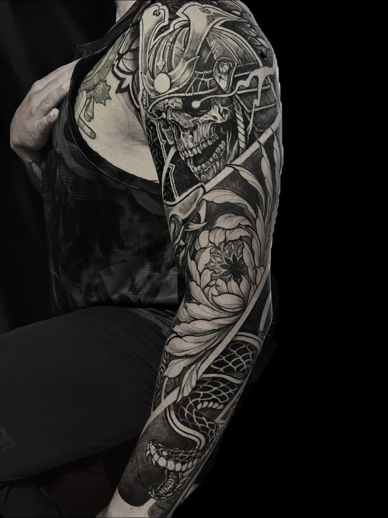 Black-and-gray sleeve tattoo on a person's arm, featuring a skull wearing a helmet, a sword, a dragon, and floral elements.