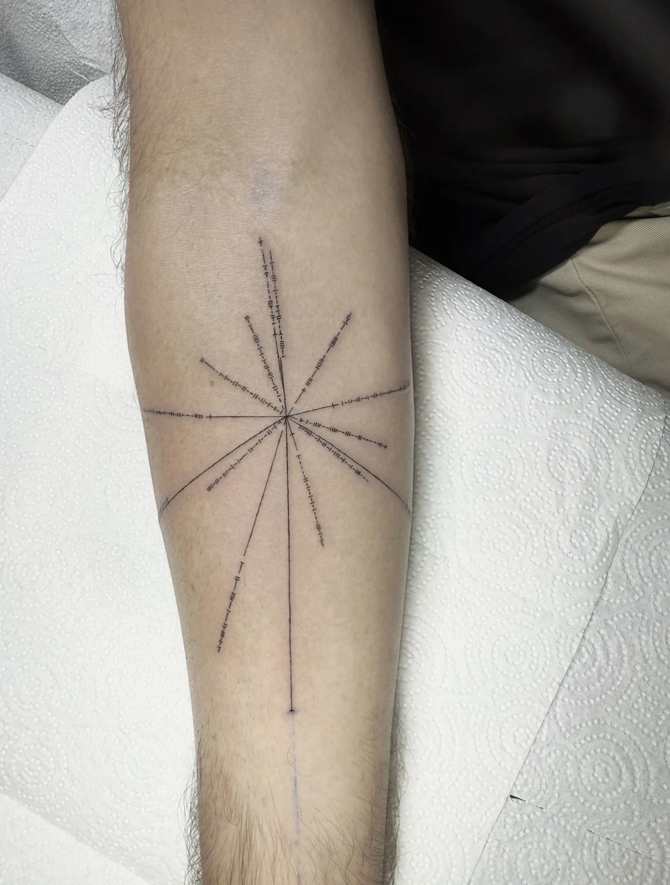 A person's calf with a geometric tattoo of lines, dots, and arrows radiating from a central point, on a white textured surface.