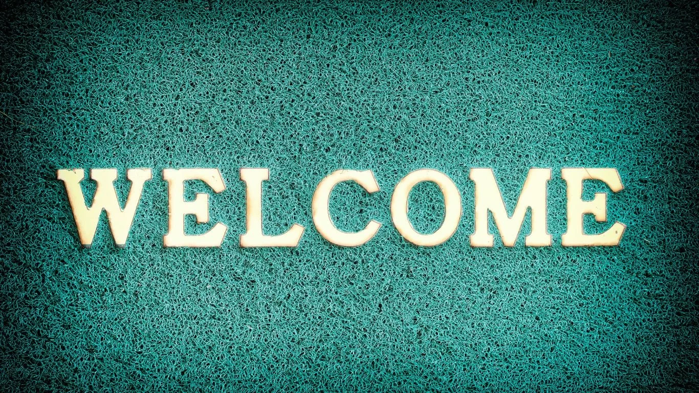 A teal welcome mat with bold lettering, symbolizing hospitality, new beginnings, and the start of a seamless real estate journey with Brit Sells The City.