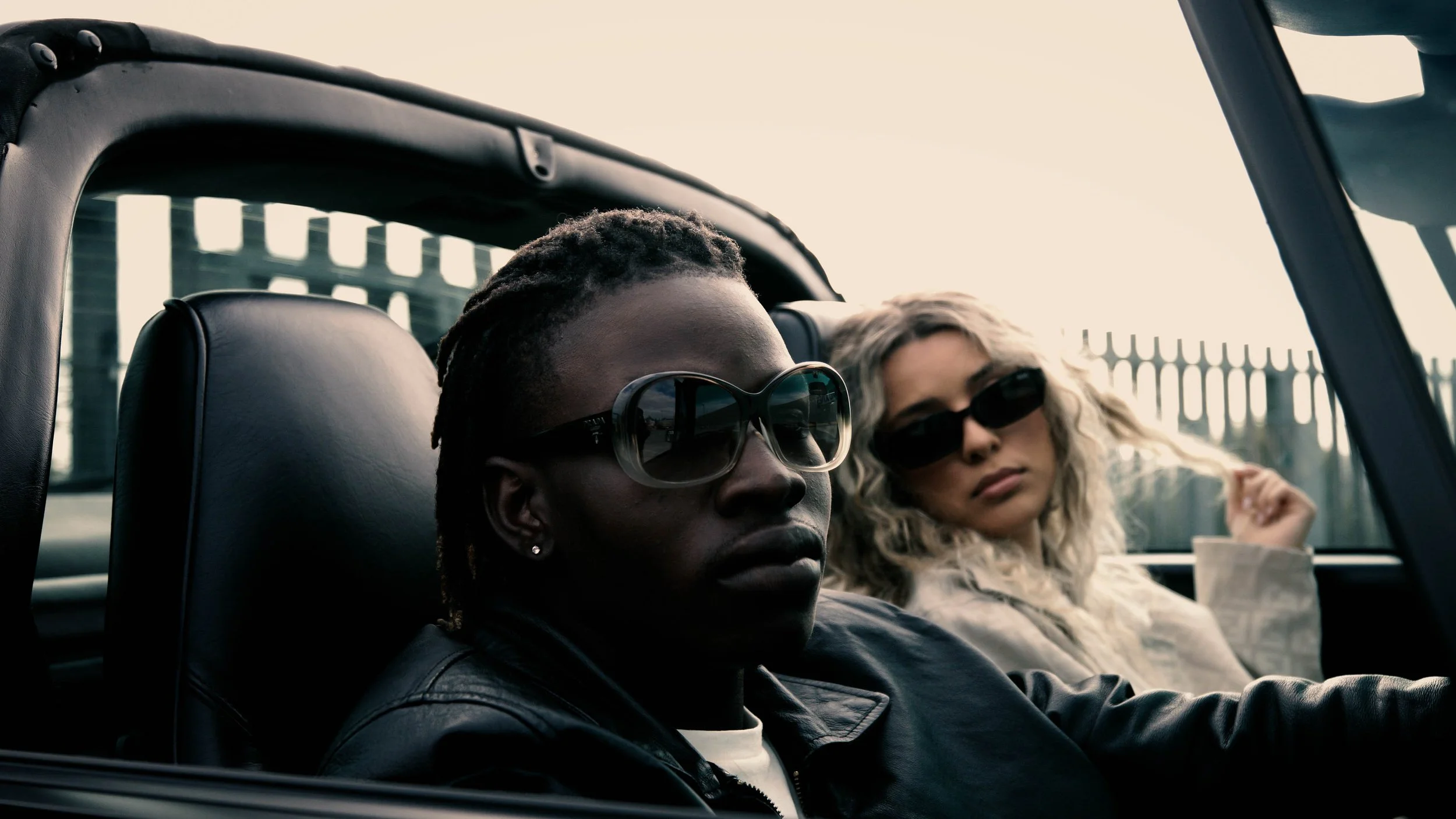 Two women with sunglasses sitting in a convertible car with the cityscape in the background.