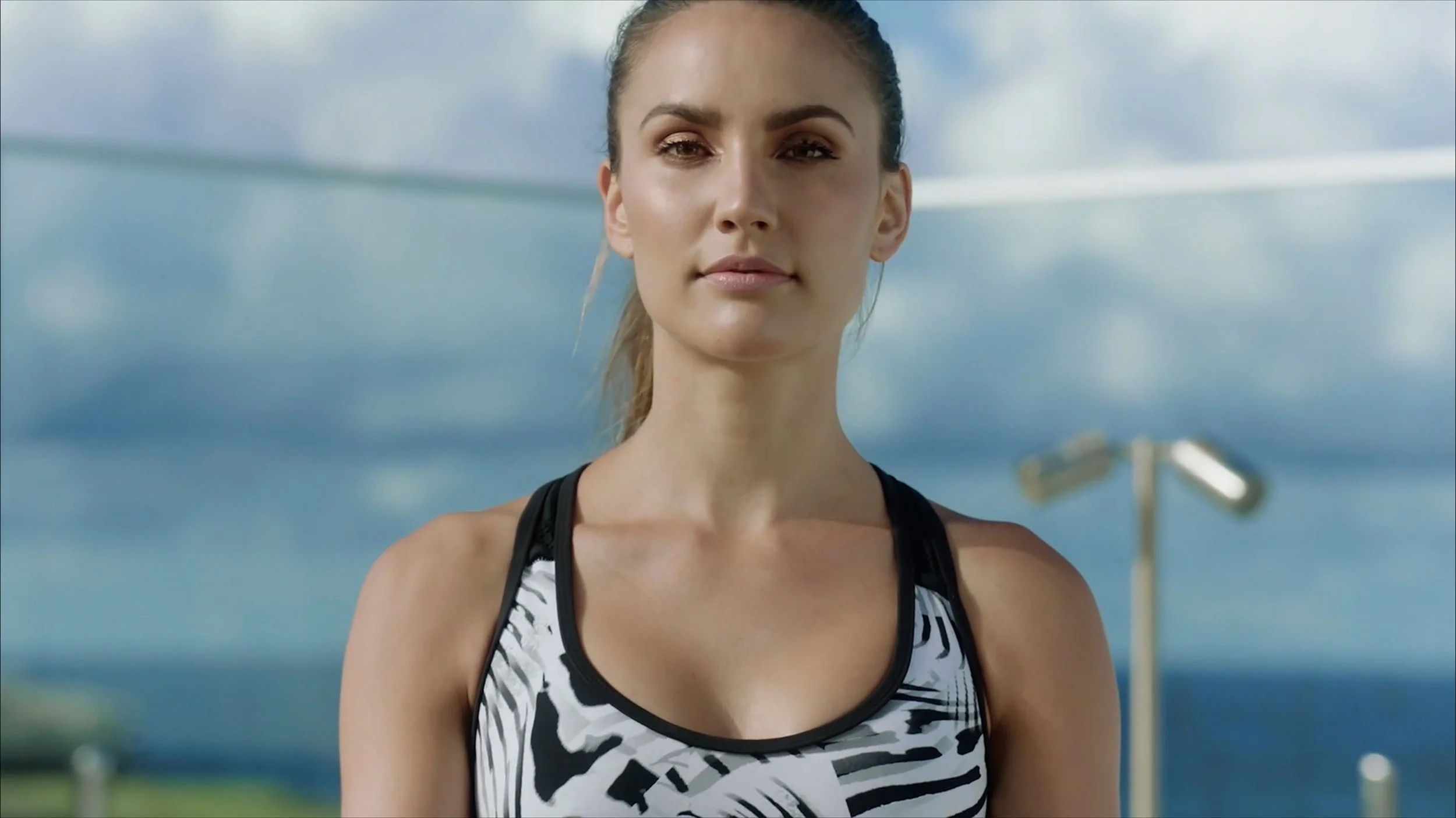 A woman in athletic wear standing outdoors near a pole with a cloudy sky background.