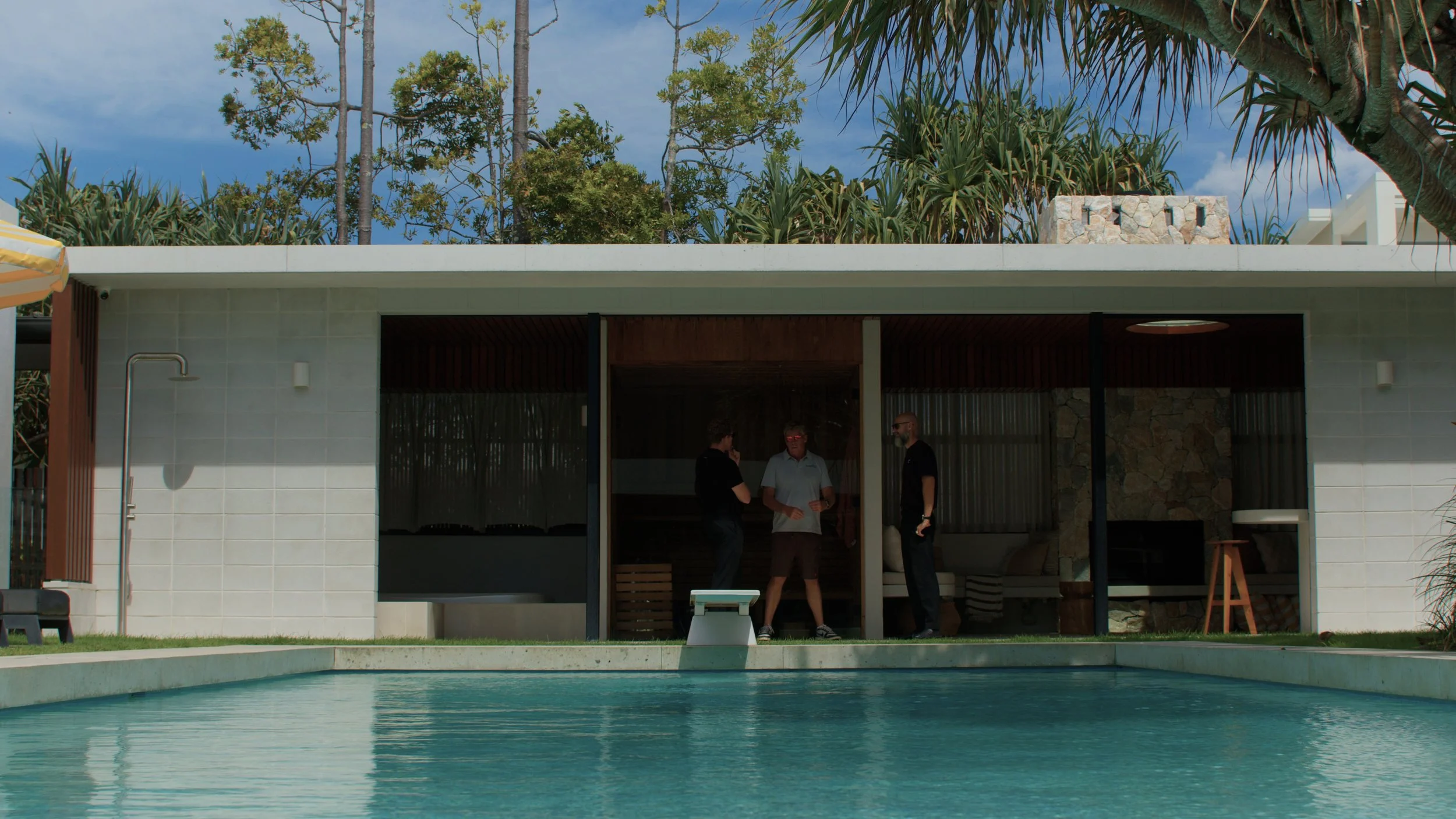 A woman with curly gray hair, glasses, and a black shirt happily reading a birthday card with a flower design and the number 10. She is sitting against a gradient background of pink, purple, and orange.