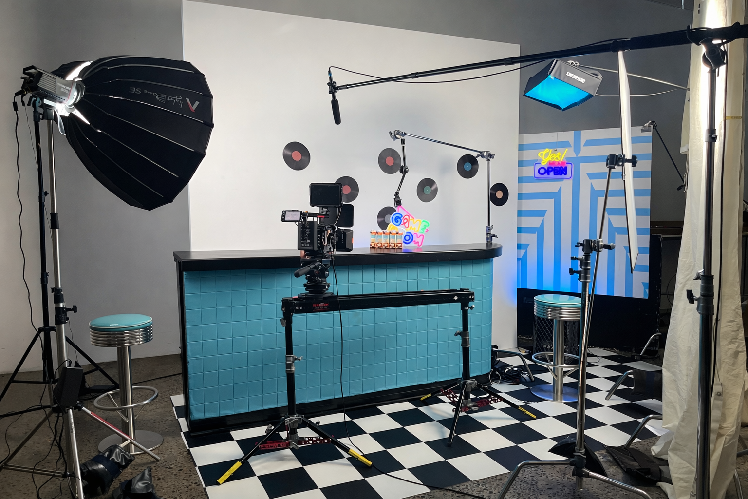 Photography studio set with lighting equipment, camera on a track, tiles, and neon signs.