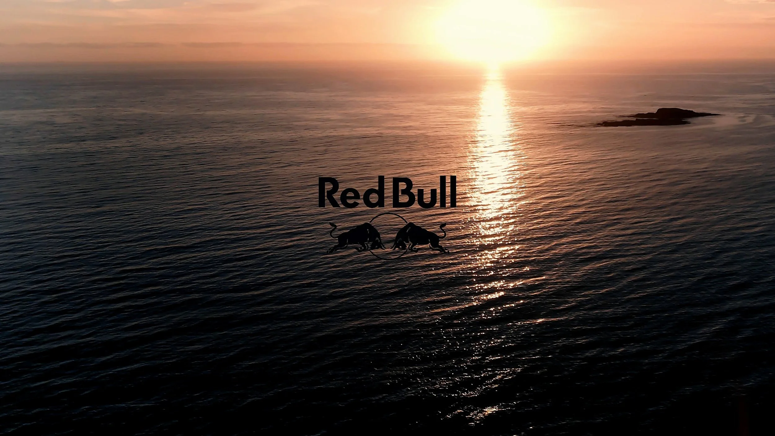 Sunset over the ocean with a logo of Red Bull and two charging bulls in silhouette.