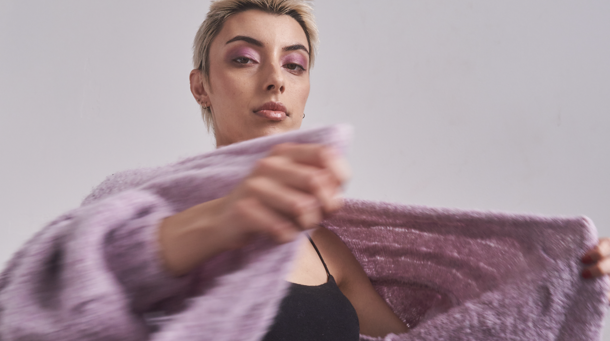 A woman with short blonde hair and pink eyeshadow holding a pink fuzzy blanket.