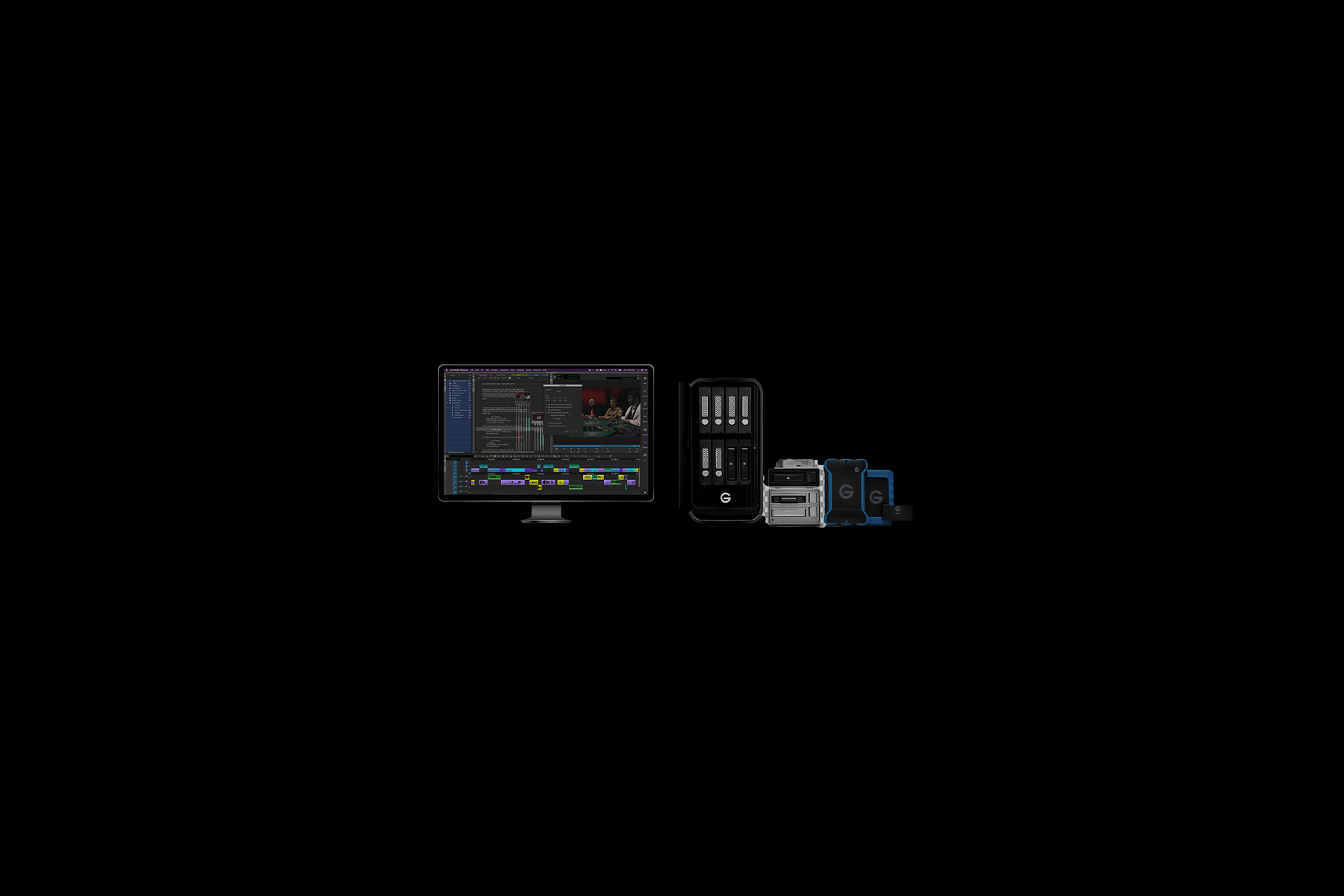 A computer setup for video editing with a monitor displaying editing software, a G-Technology storage array, external drives, and mobile device accessories against a black background.