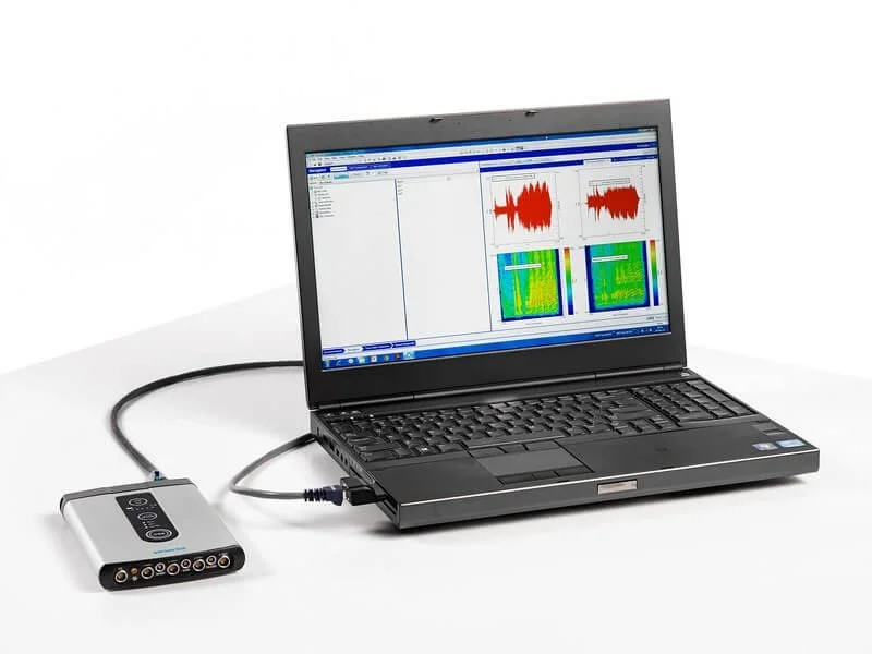 Laptop displaying audio analysis software connected to a device via cable.