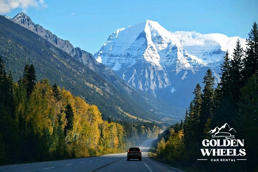 Car driving on a mountain highway with a snow-capped peak in the background and trees on both sides